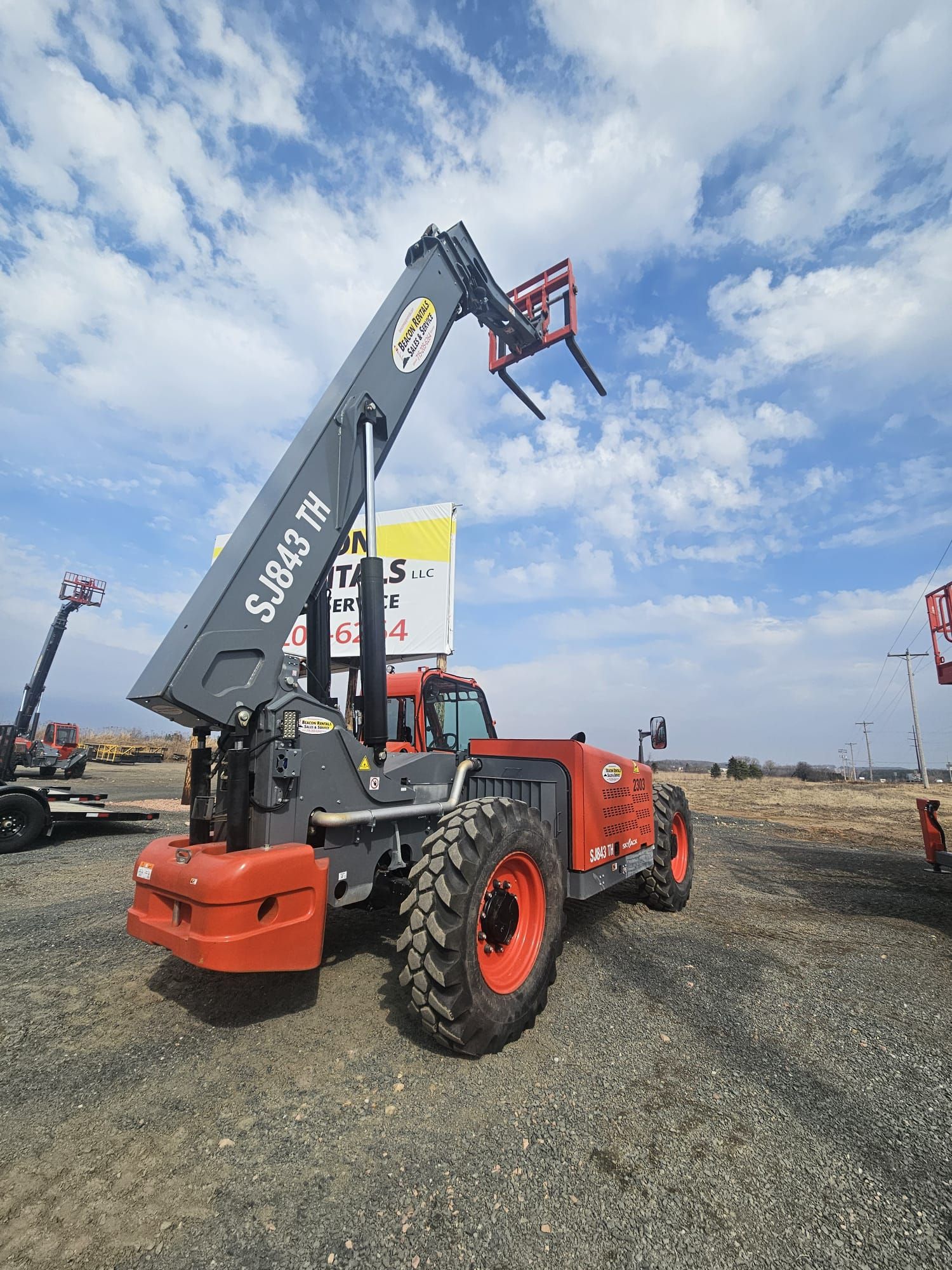 Orange and gray telescopic forklift with forks extended against a cloudy sky.