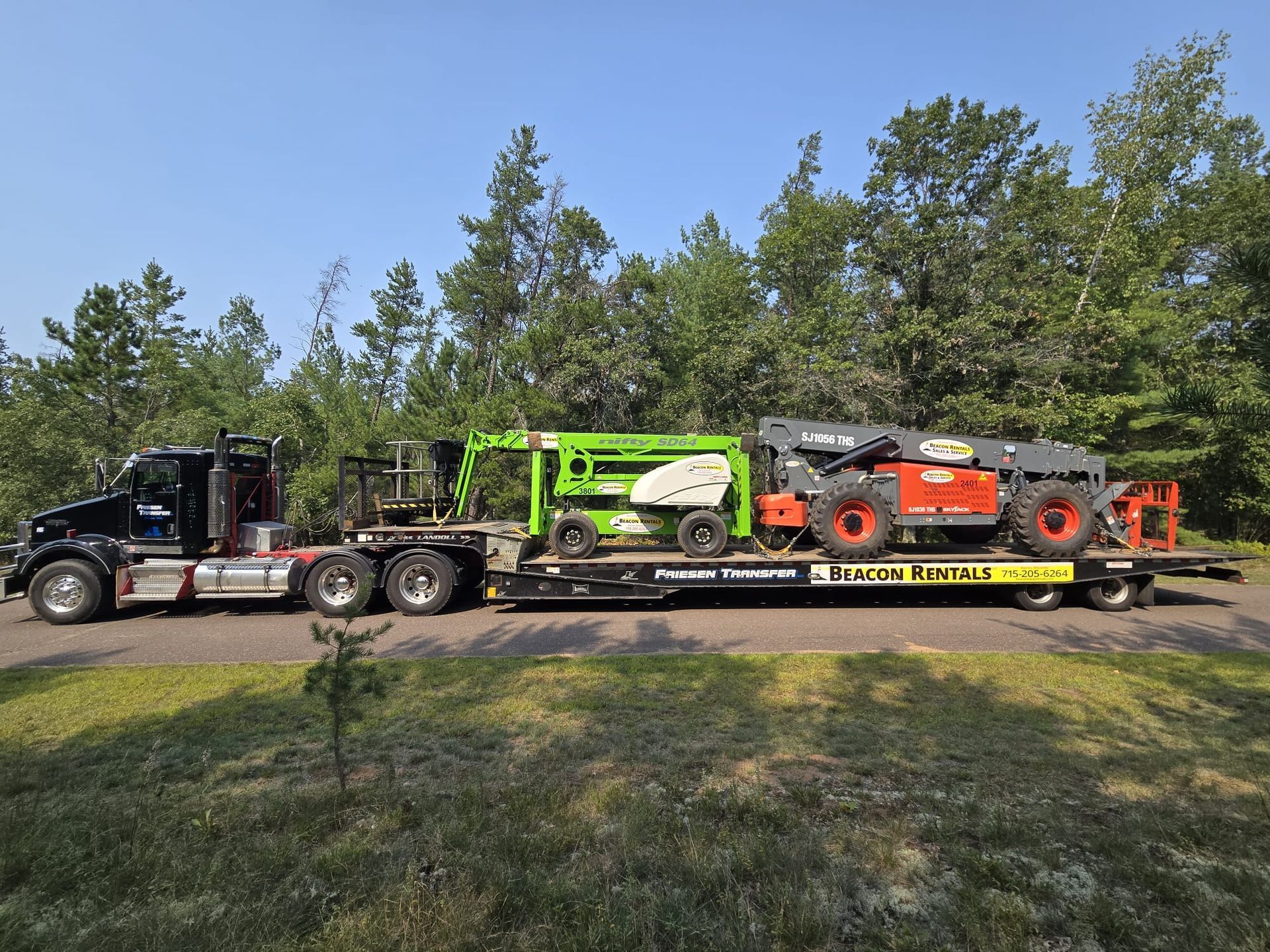 Truck hauling two pieces of heavy construction equipment on a trailer along a road.