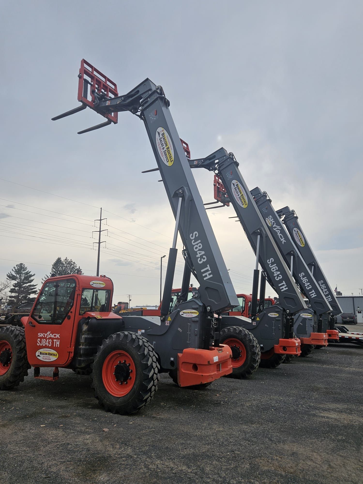 Orange and gray telescopic forklifts parked in a row, under an overcast sky.