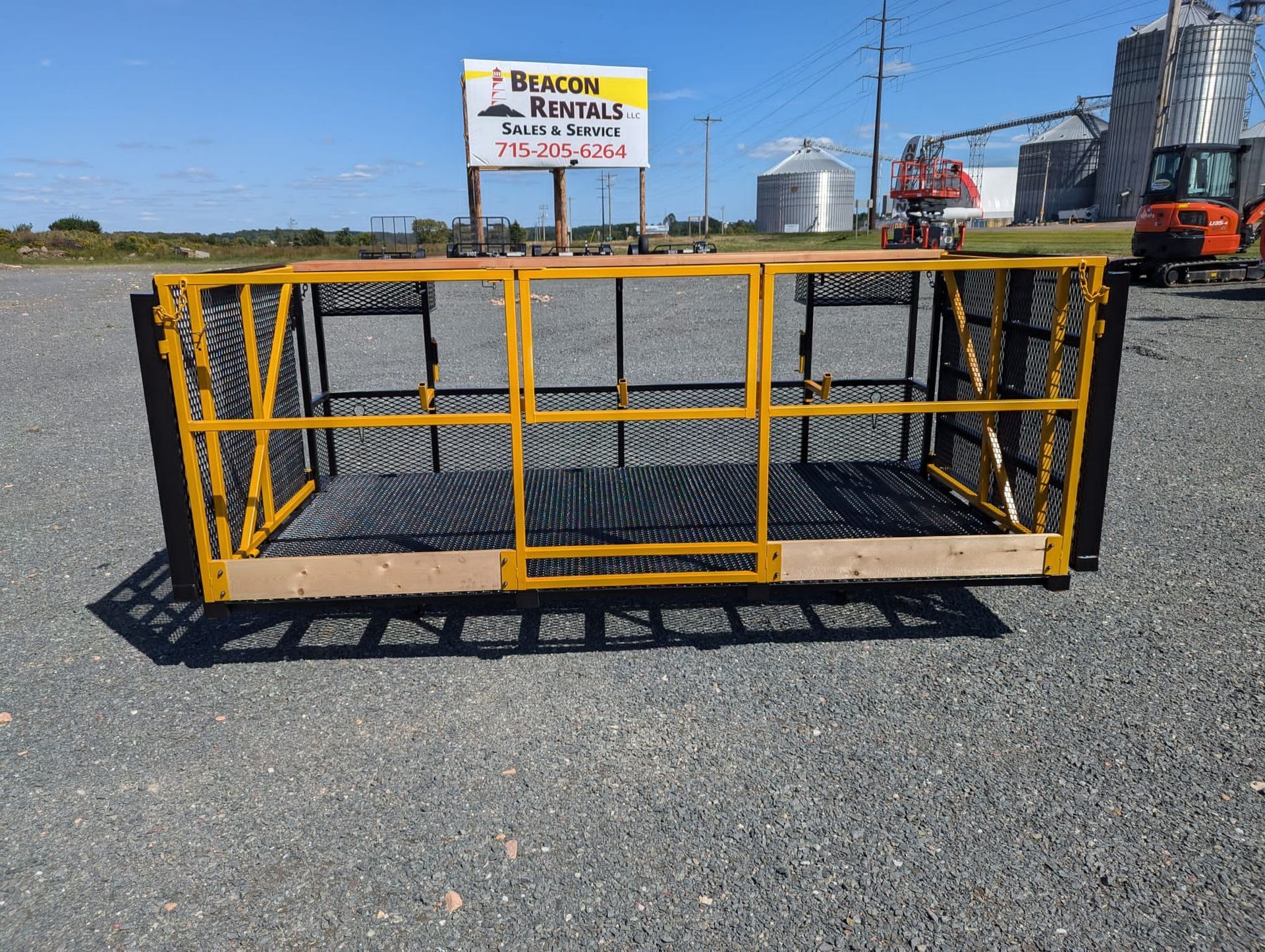 Yellow and black aerial work platform on gravel; Beacon Rentals sign in background.