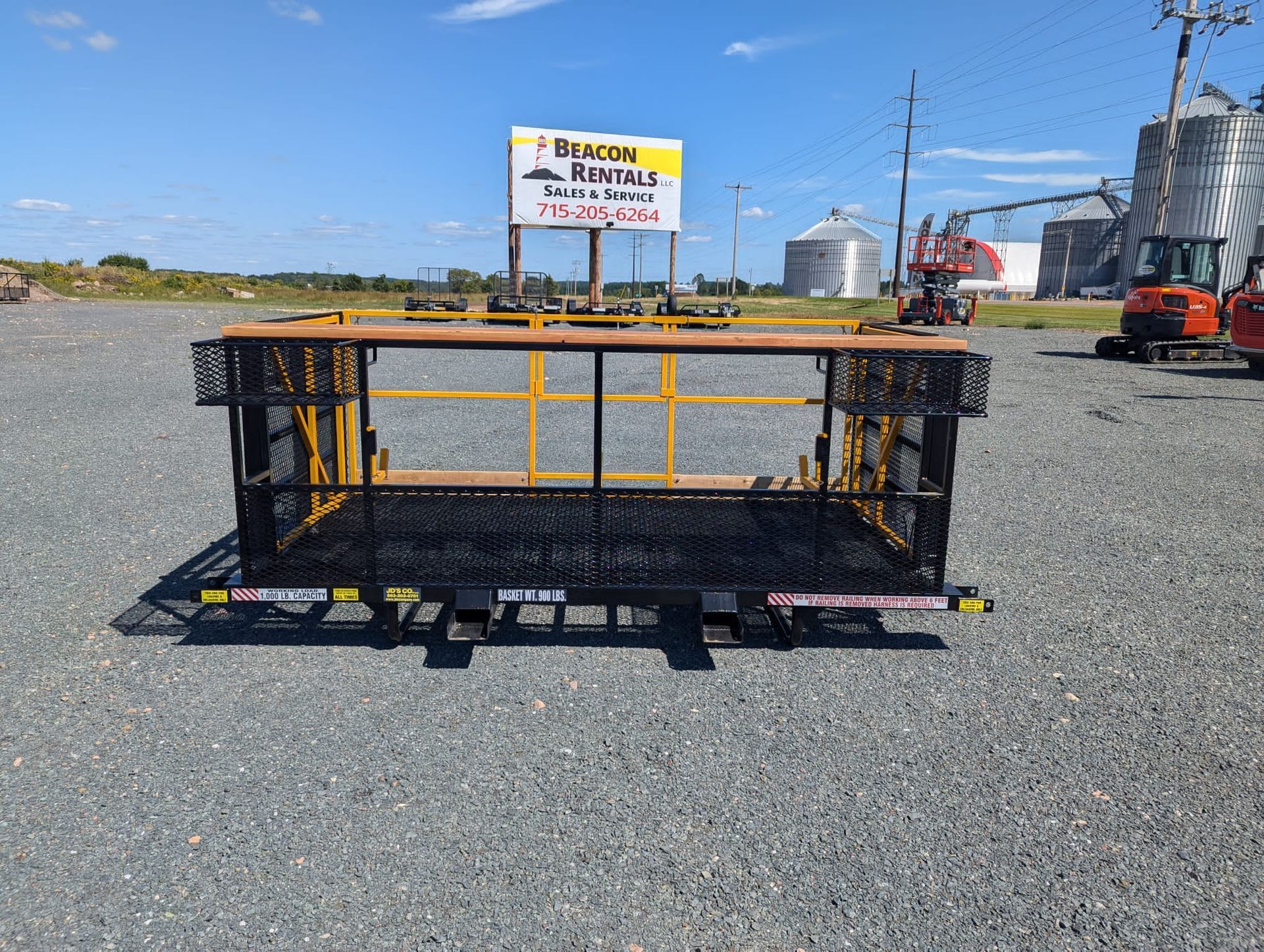 Black and yellow equipment basket on trailer, outdoor gravel setting. Sign in background.