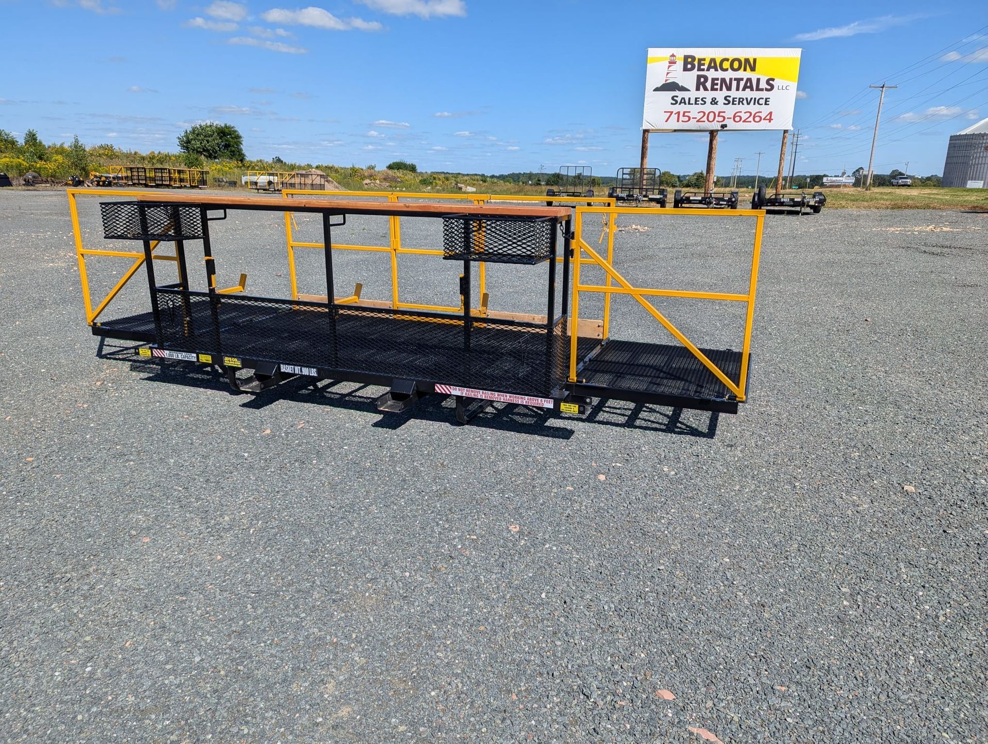 Yellow metal scaffolding platform on gravel, outdoors, under a blue sky, with a rental sign in the background.