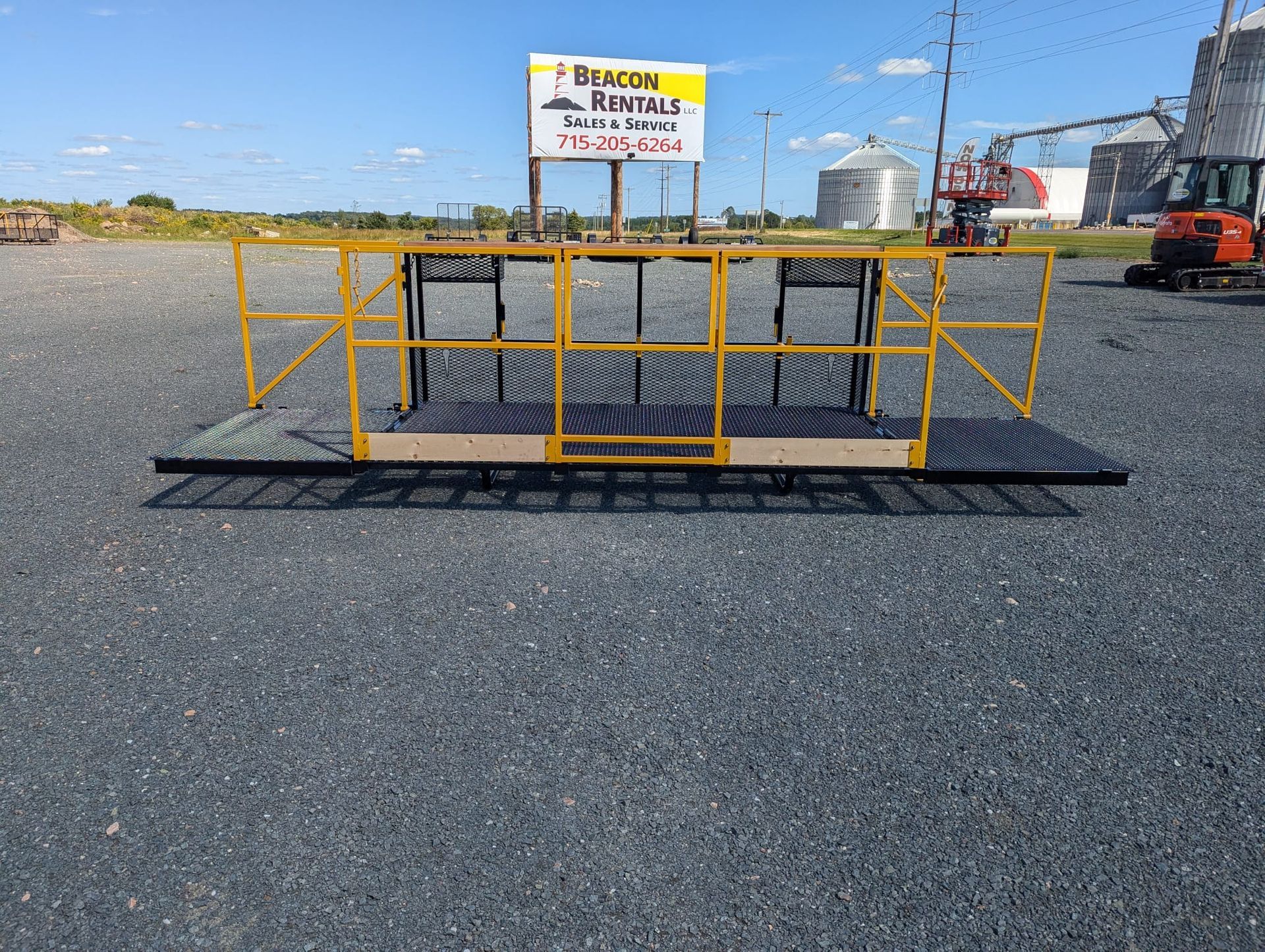 Yellow and black aerial work platform on gravel; sign for Beacon Rentals in background.