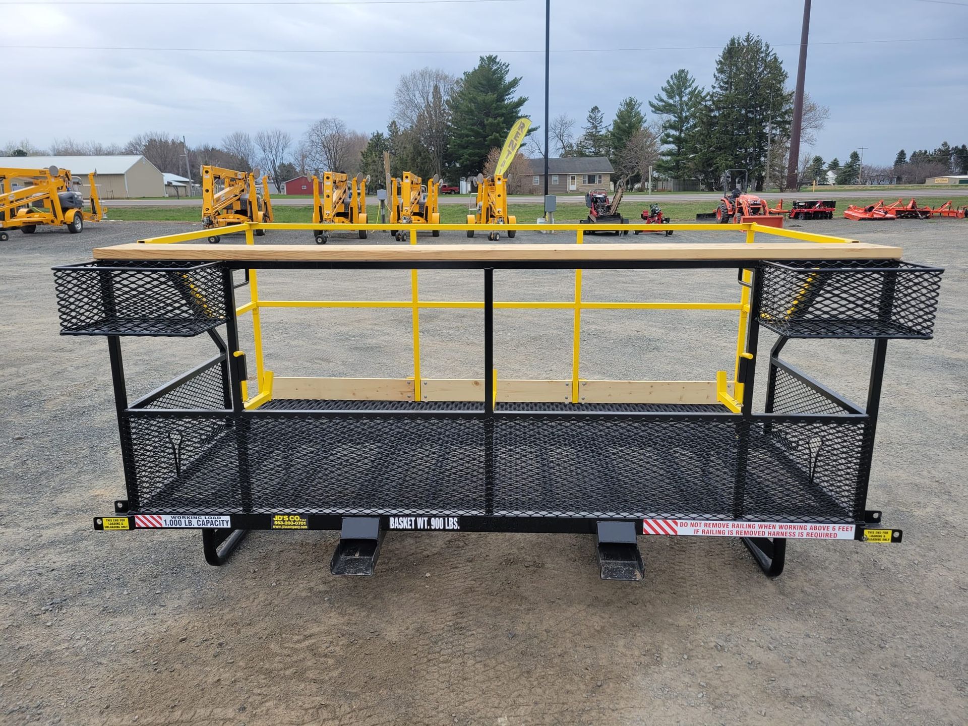 Black and yellow forklift platform with safety rails, metal mesh, and storage baskets; outdoors.