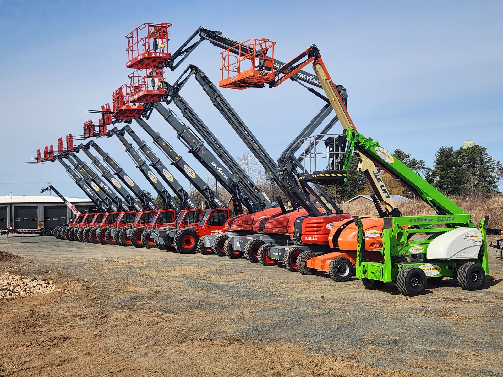 A row of aerial work platforms; most are red, one is green, all are extended in the air, outside on a sunny day.