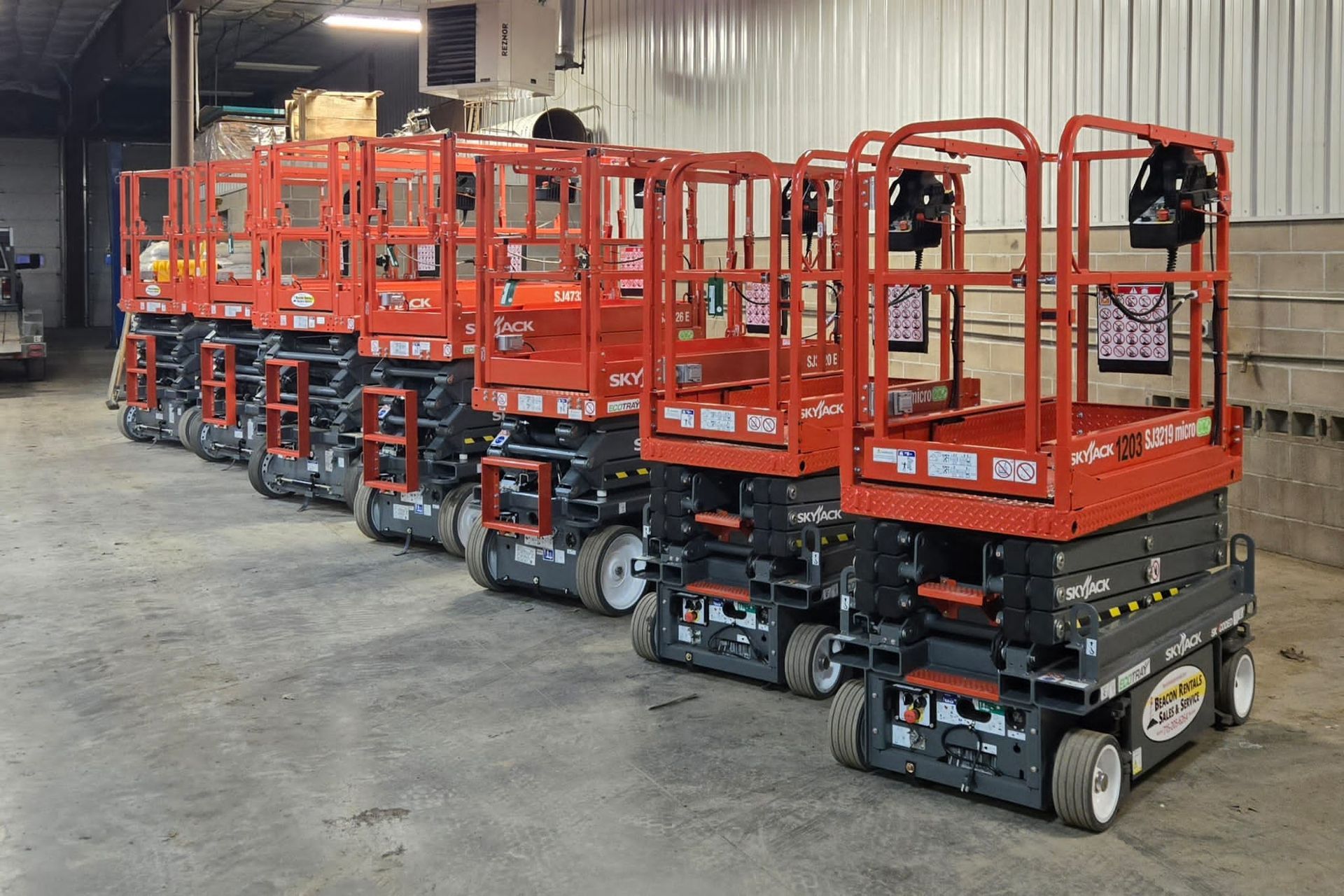 Row of red and black scissor lifts inside a warehouse.