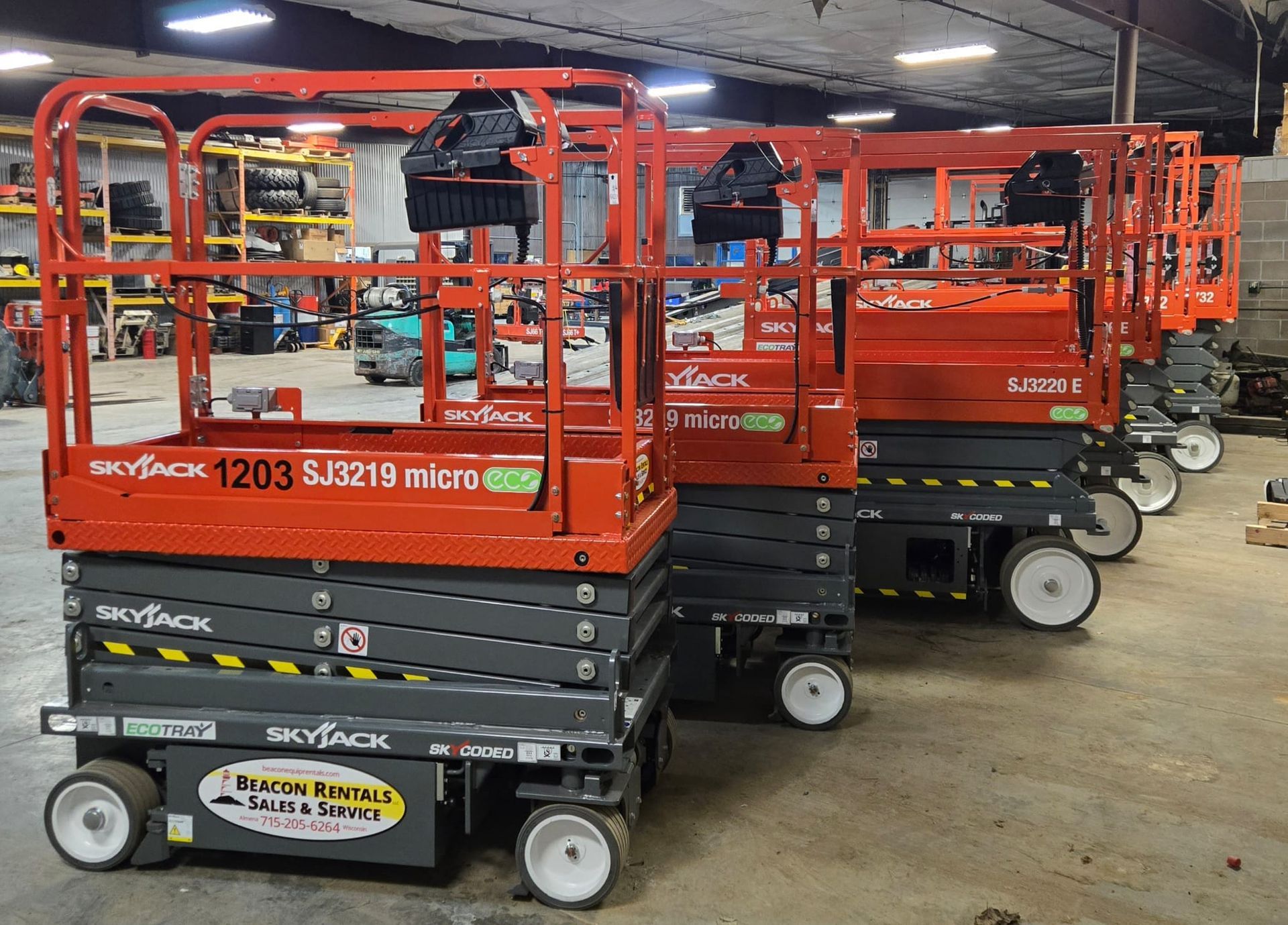 Several orange and gray Skyjack scissor lifts parked in a warehouse.