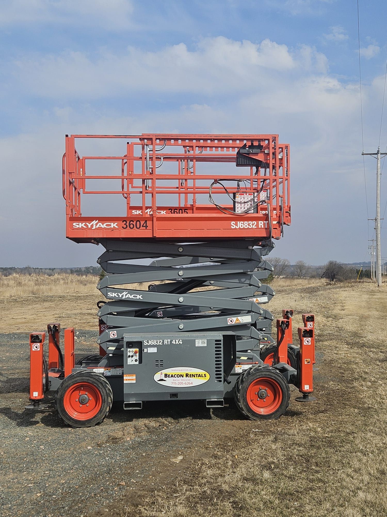 A tall, orange and gray aerial lift on a grassy field with a cloudy sky.