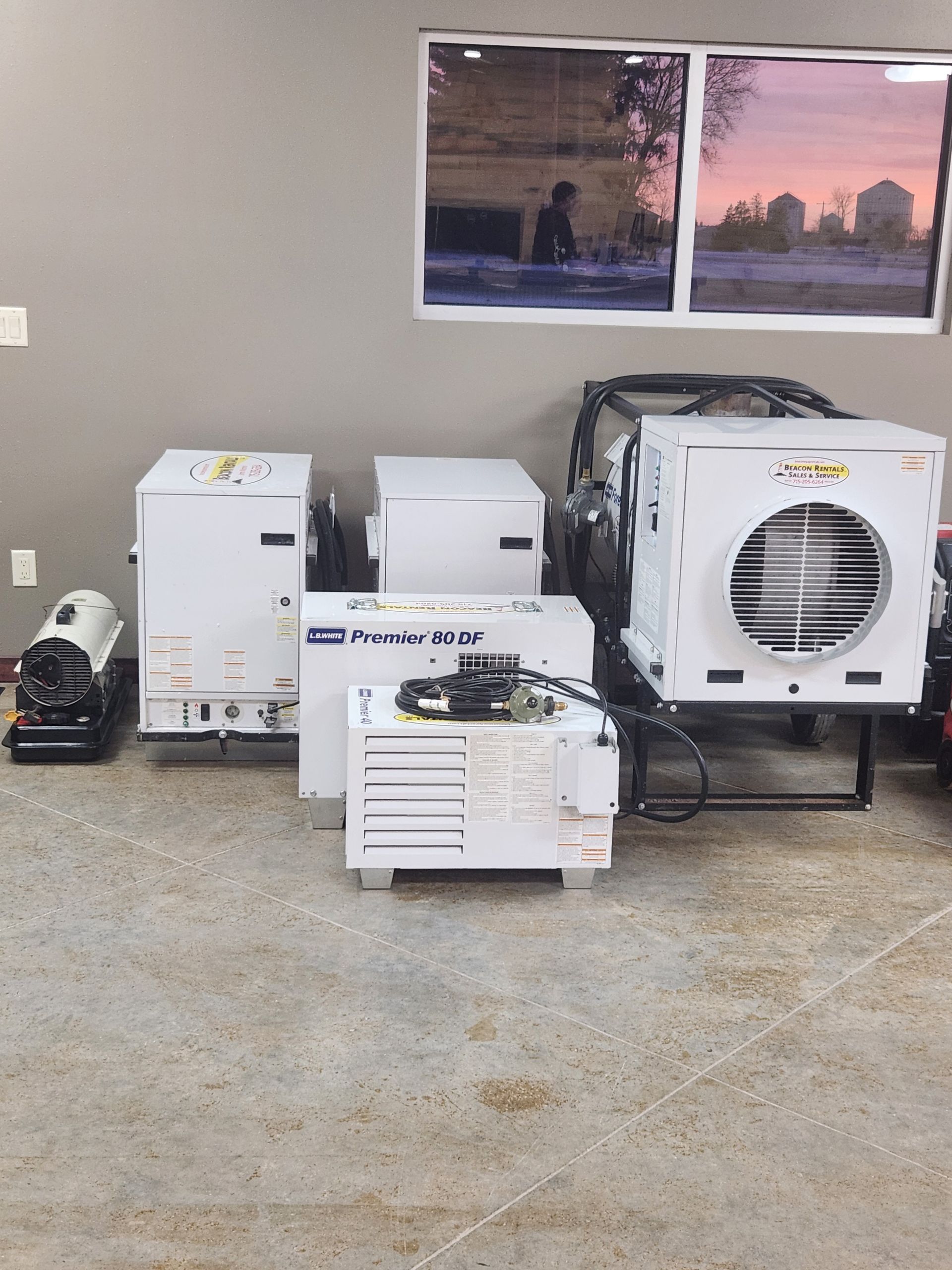 Several white industrial cooling units and a black machine on a concrete floor near a window.