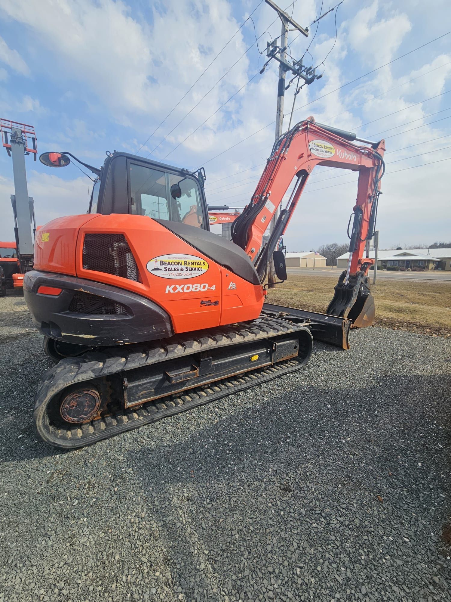 Orange Kubota excavator on gravel, under a blue sky.