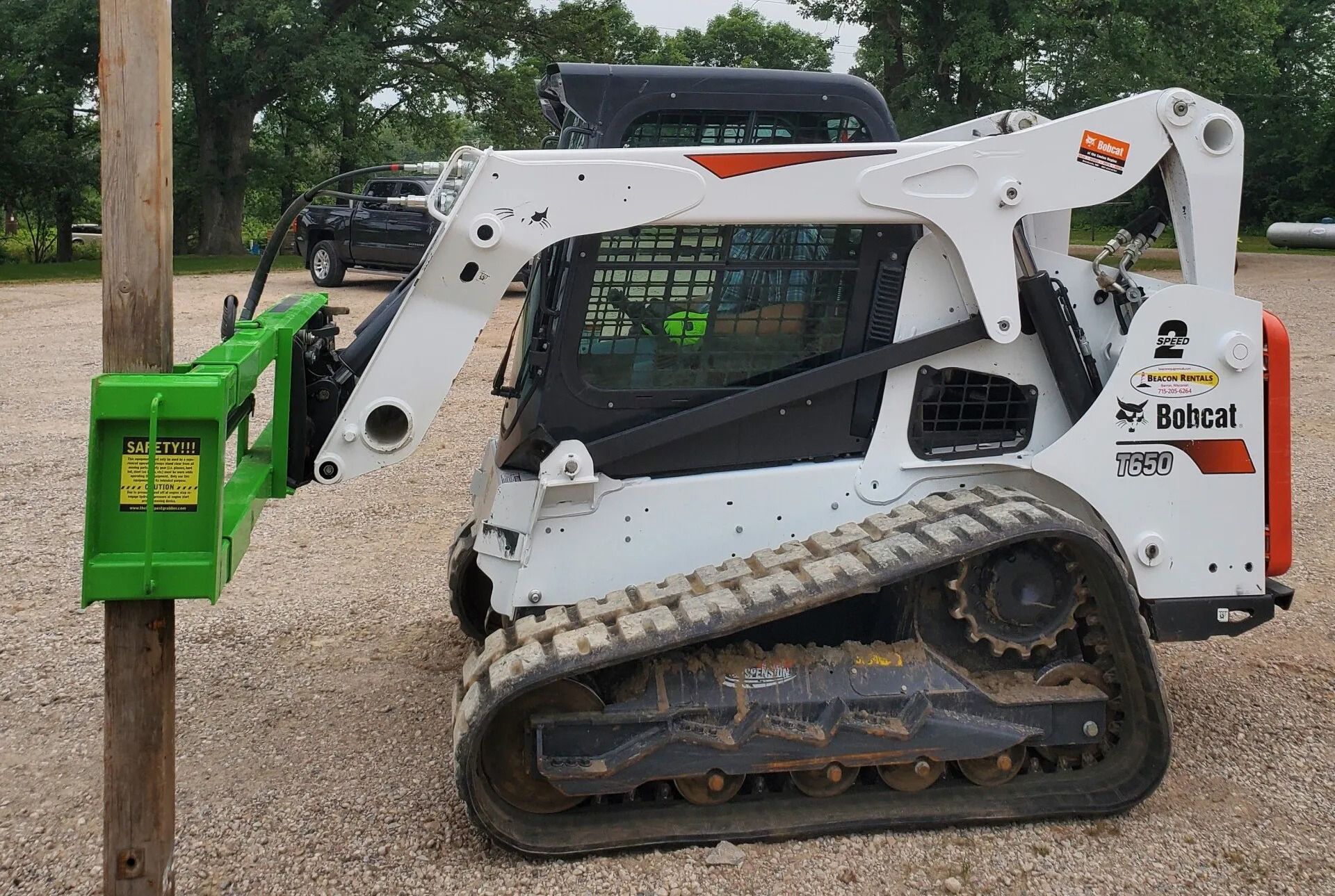 White Bobcat skid steer with green post driver attachment removing a wooden pole.