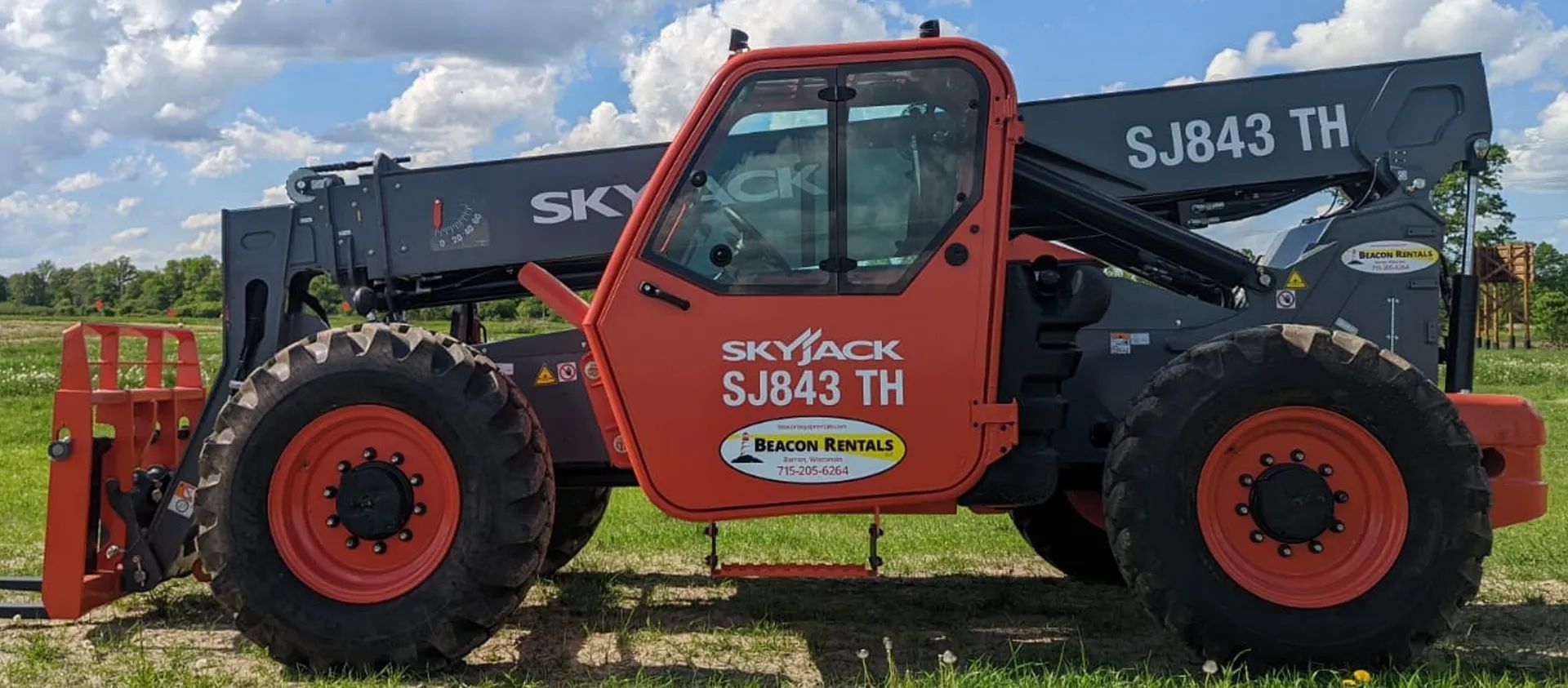 An orange and gray Skyjack SJ843 TH telehandler on green grass.