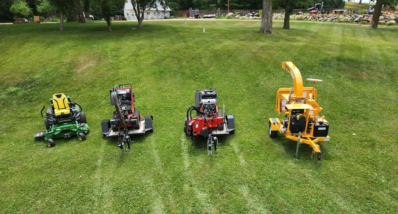 Four wood chippers on a grassy field, various colors and sizes.
