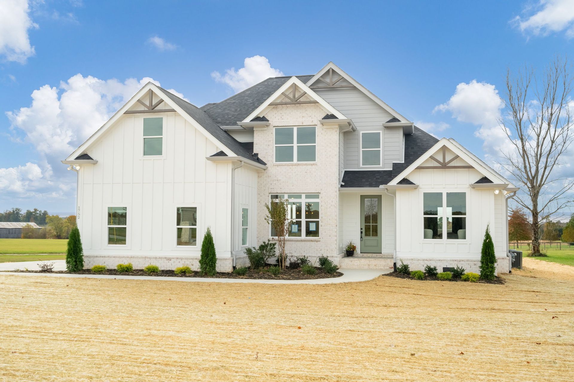 A large white house with a black roof is sitting on top of a dirt field.