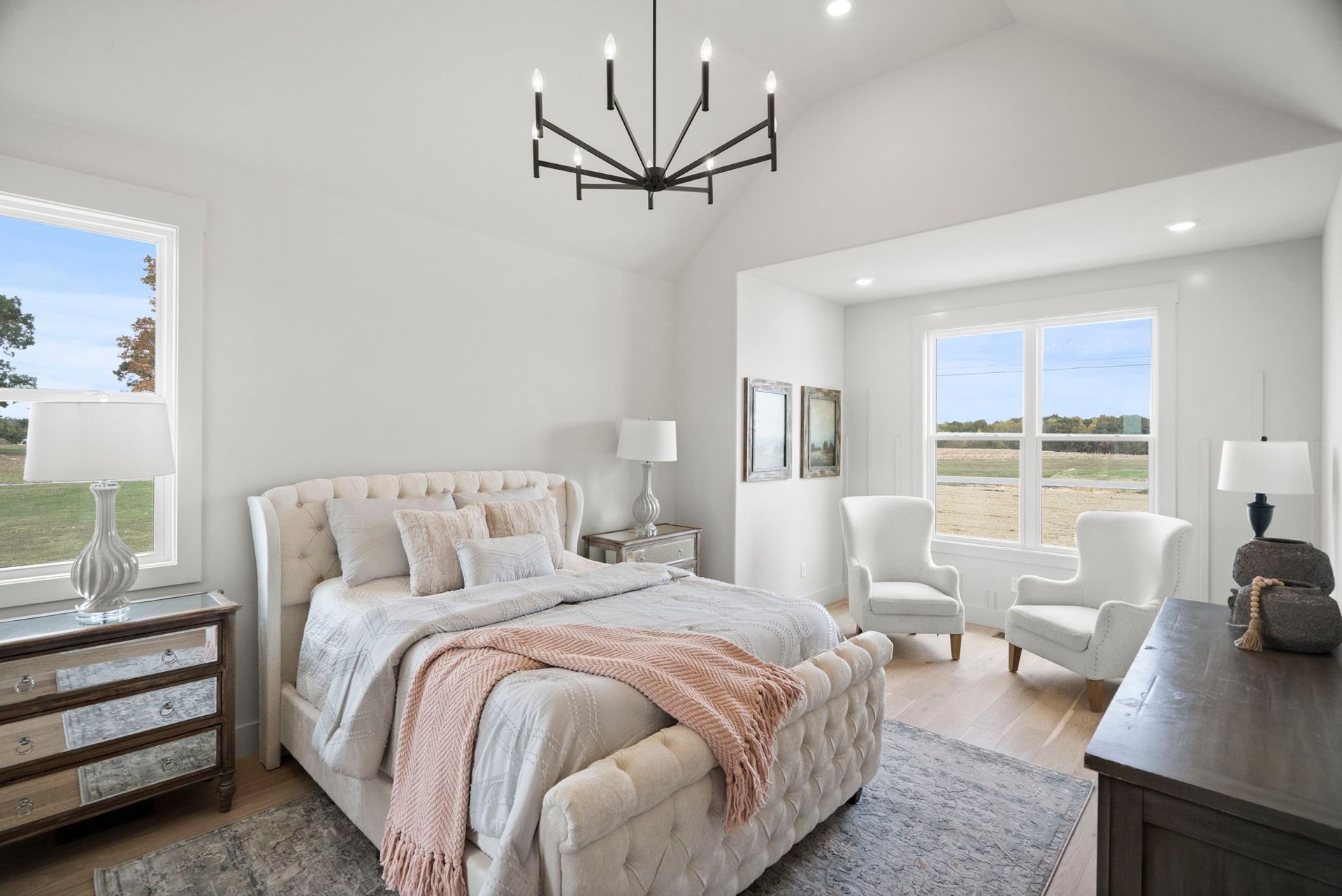 A bedroom with a bed , chairs , dresser and chandelier.