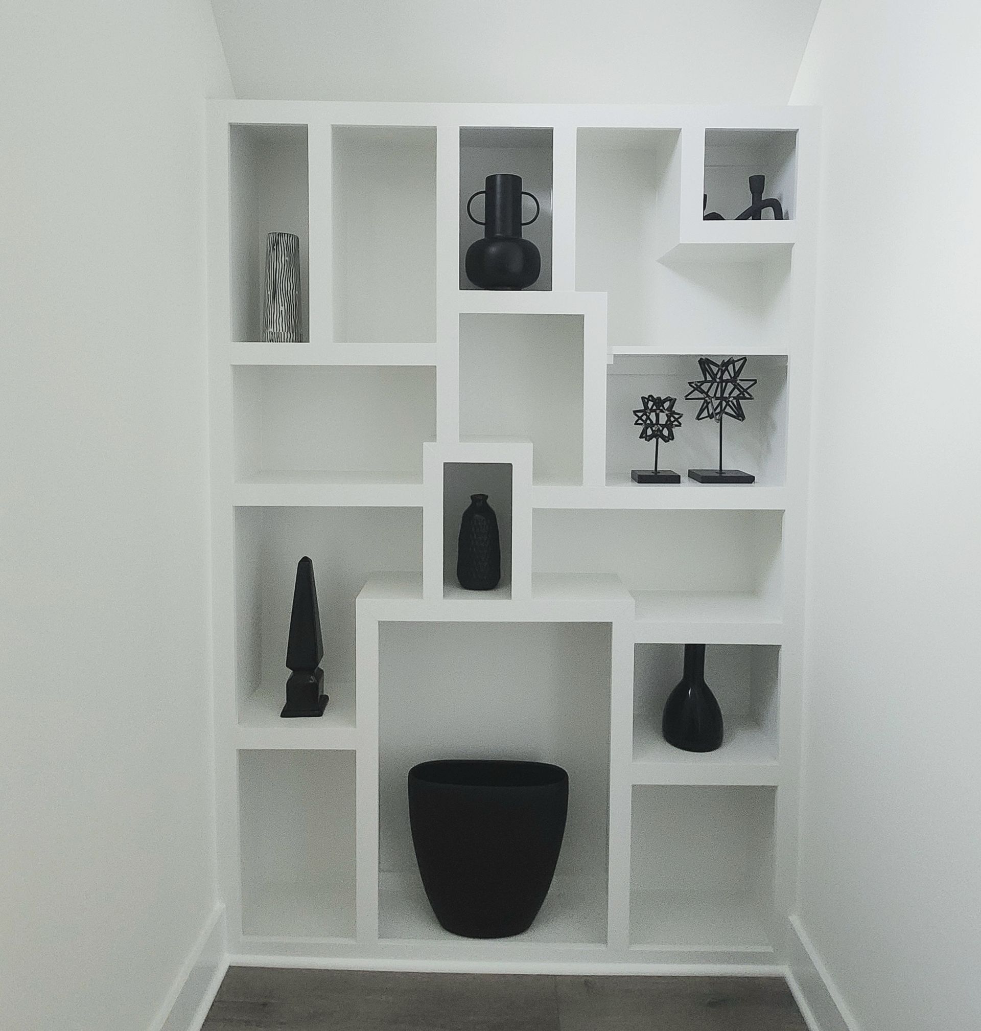 A white shelf with black vases and candles on it