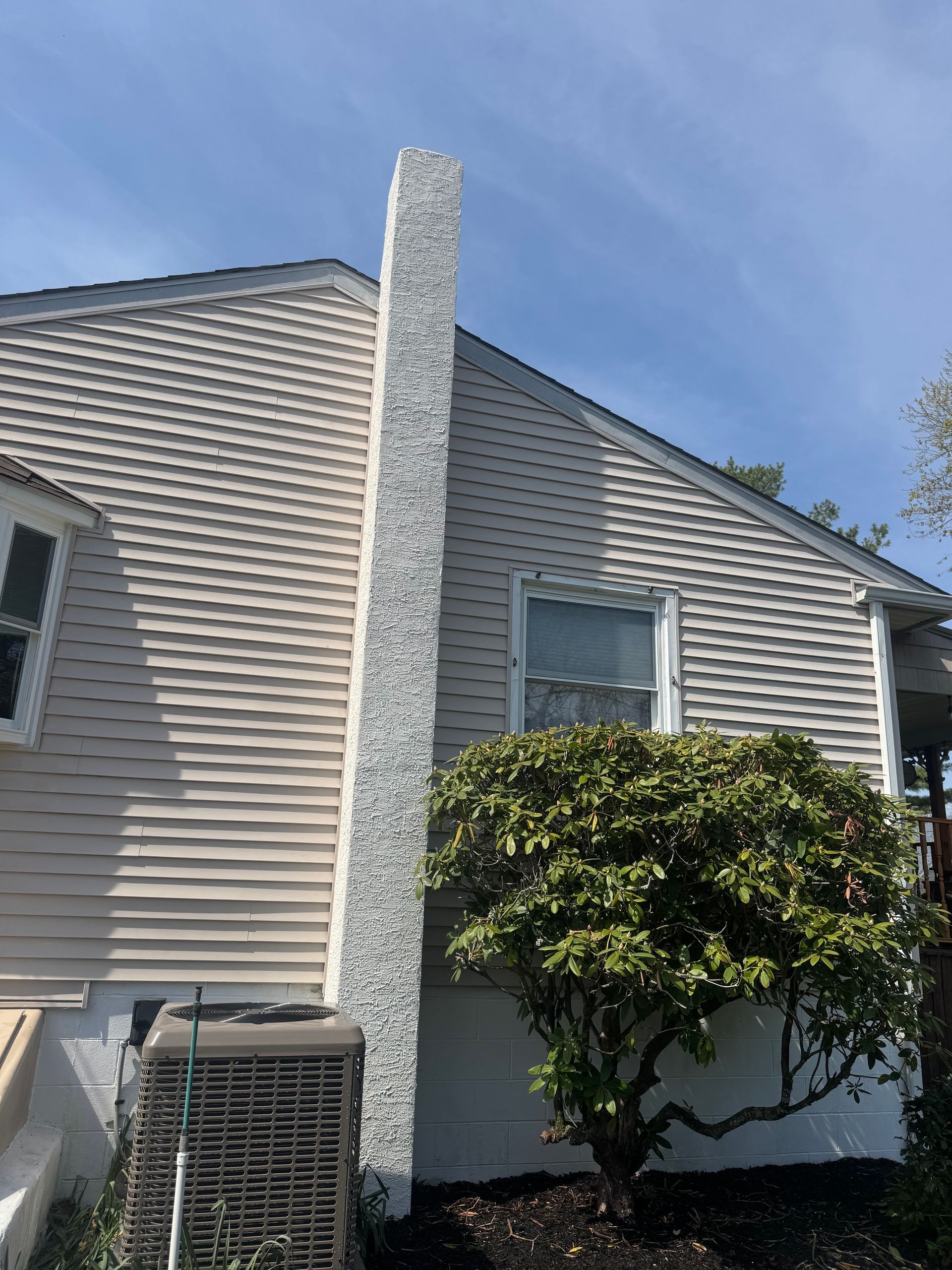 A house with a chimney on the side of it and a tree in front of it.