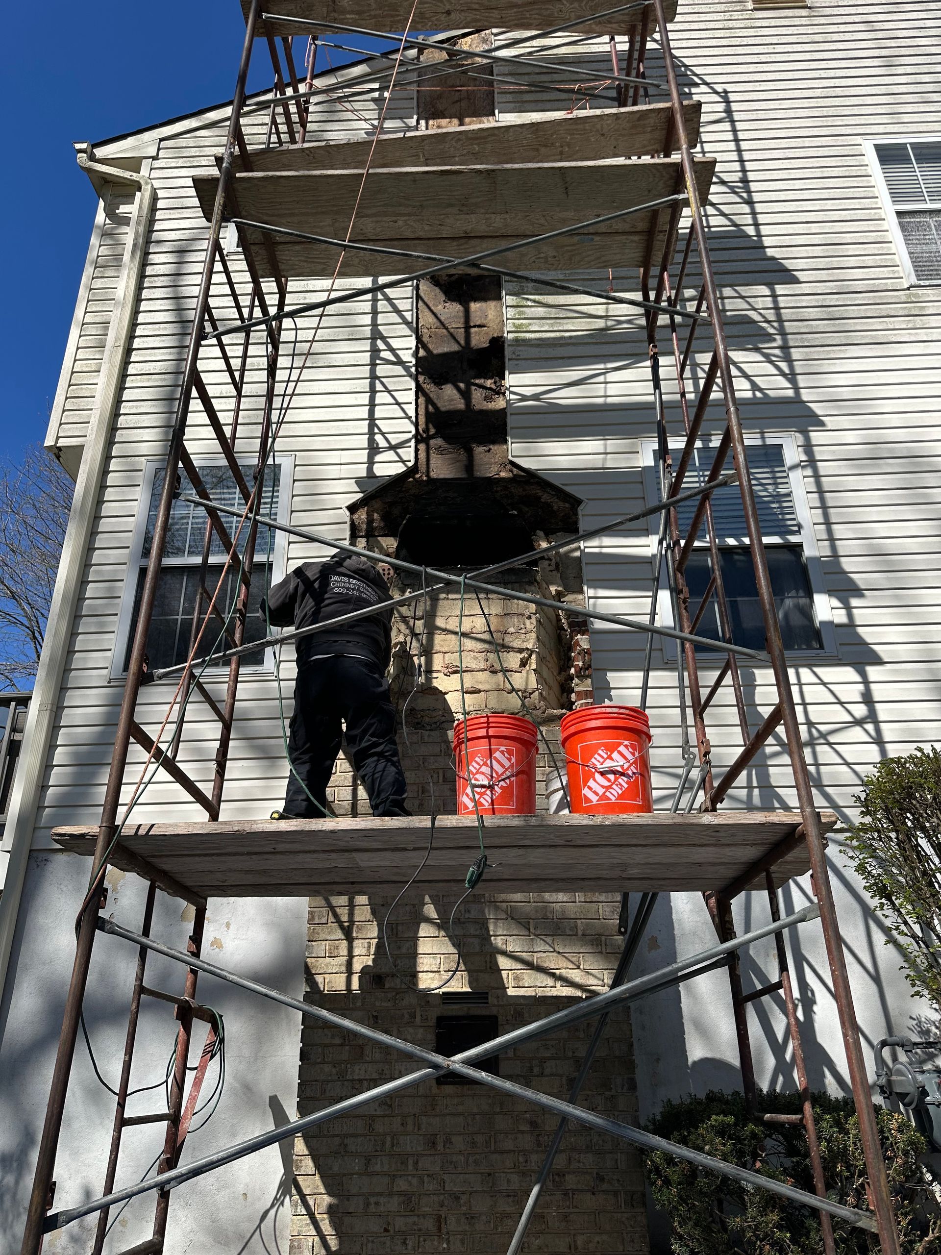 A man is standing on a scaffolding in front of a house.