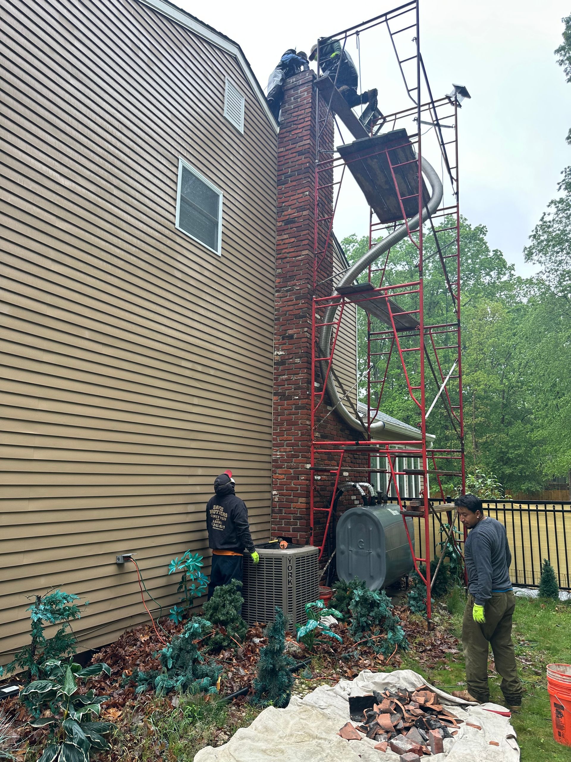 A group of men are working on a chimney on the side of a house.