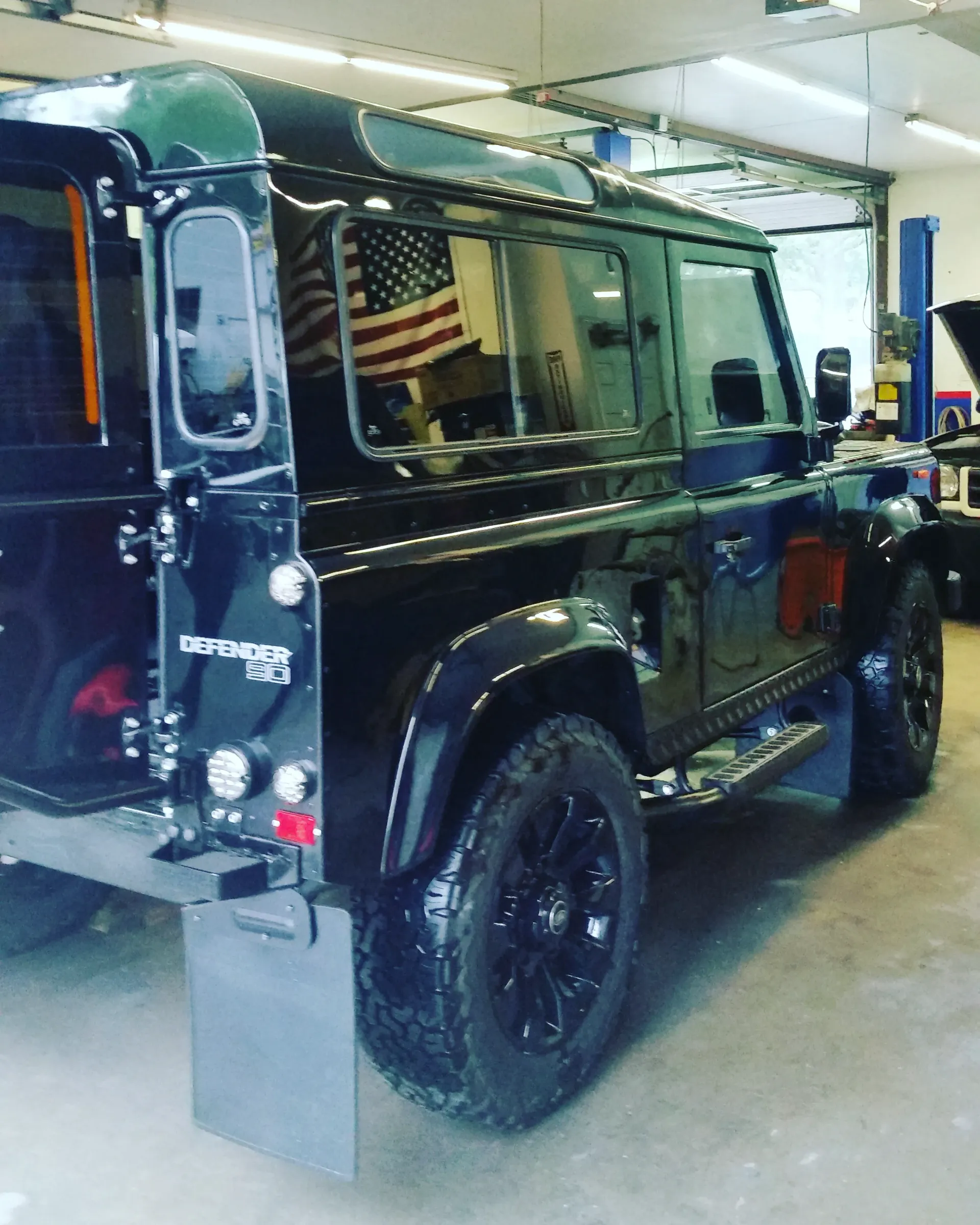 A black land rover defender is parked in a garage