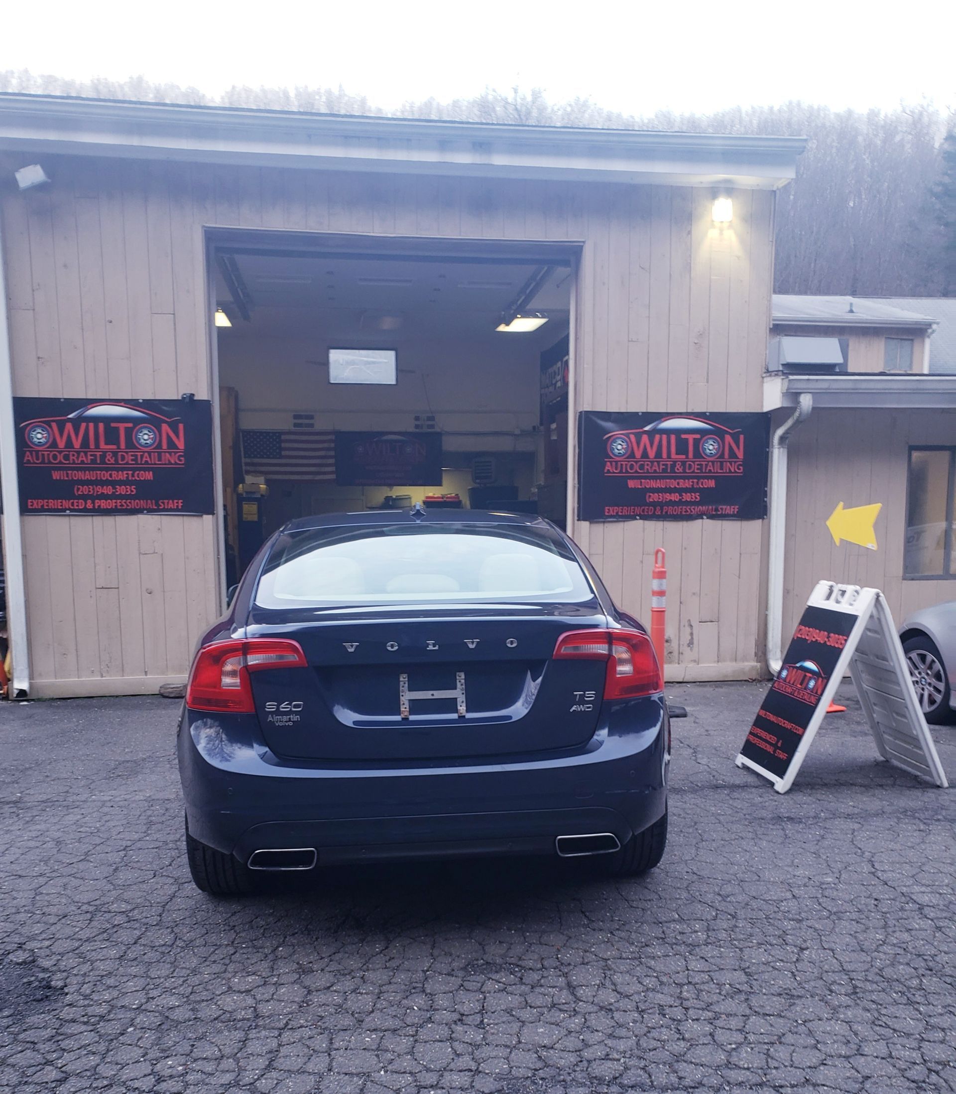 A black car is parked in front of a car dealership.