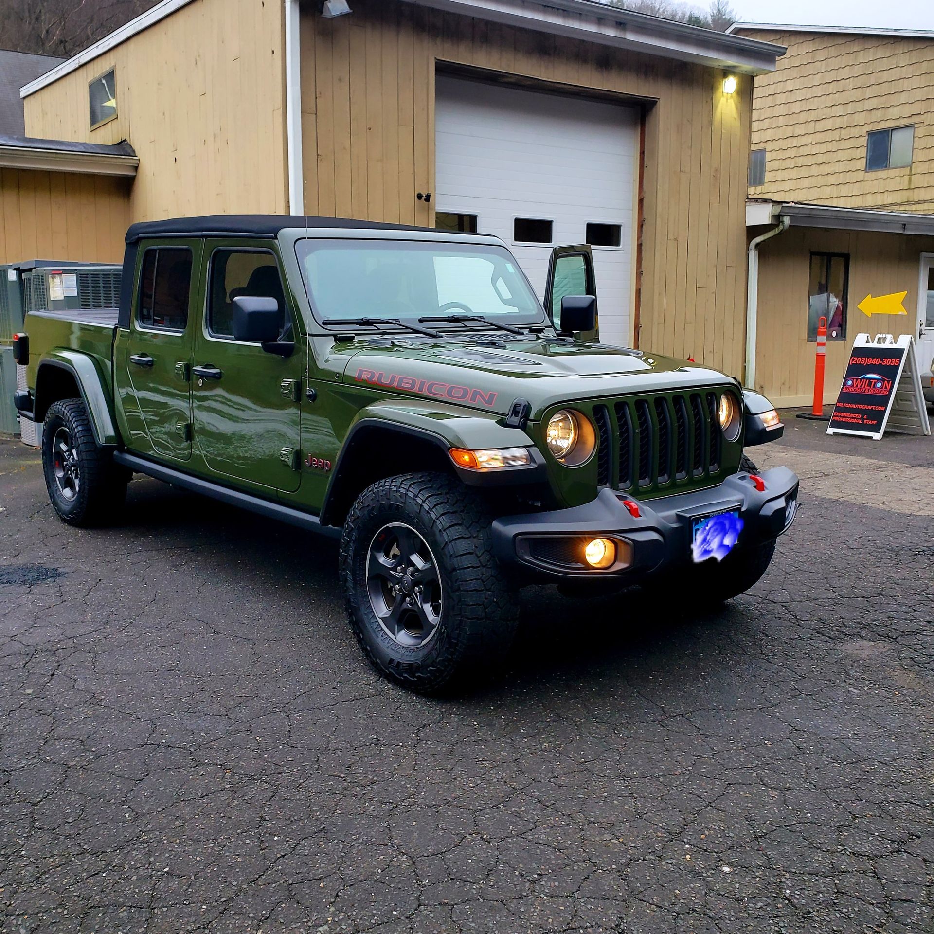 A green jeep is parked in front of a garage