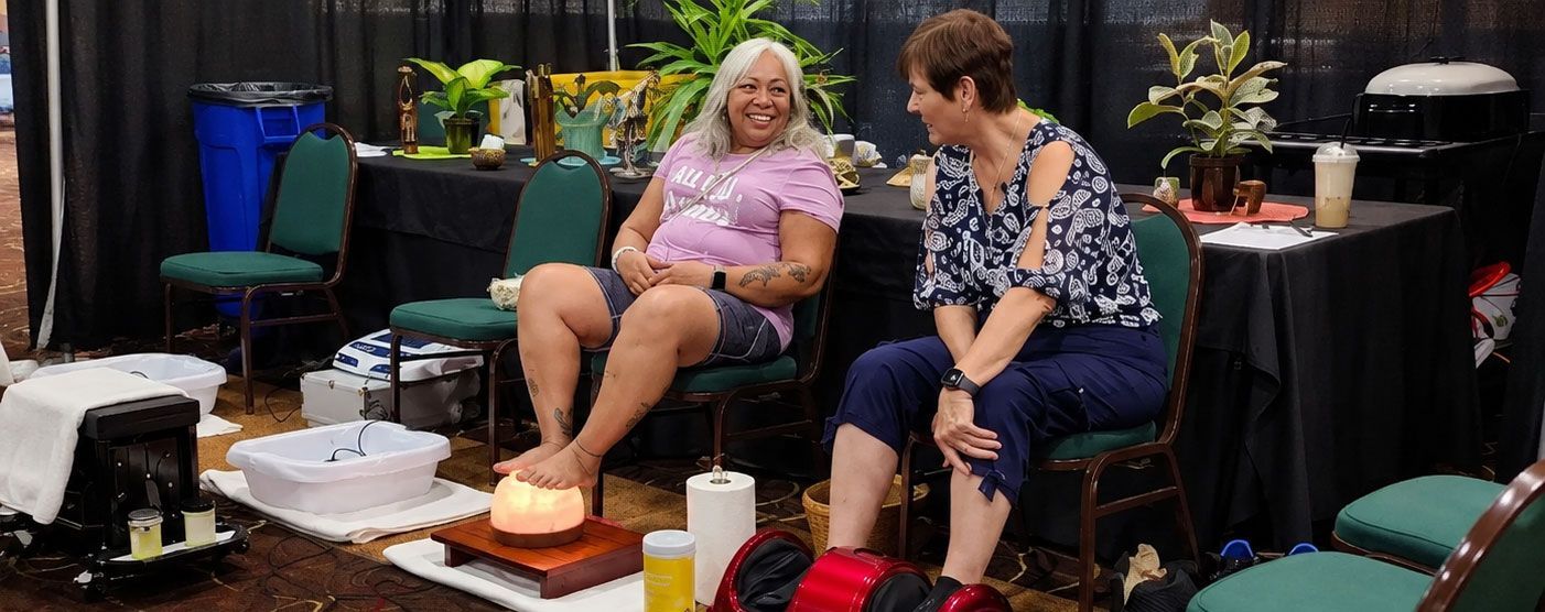 Two women seated at a table, smiling and chatting in a casual indoor setting.