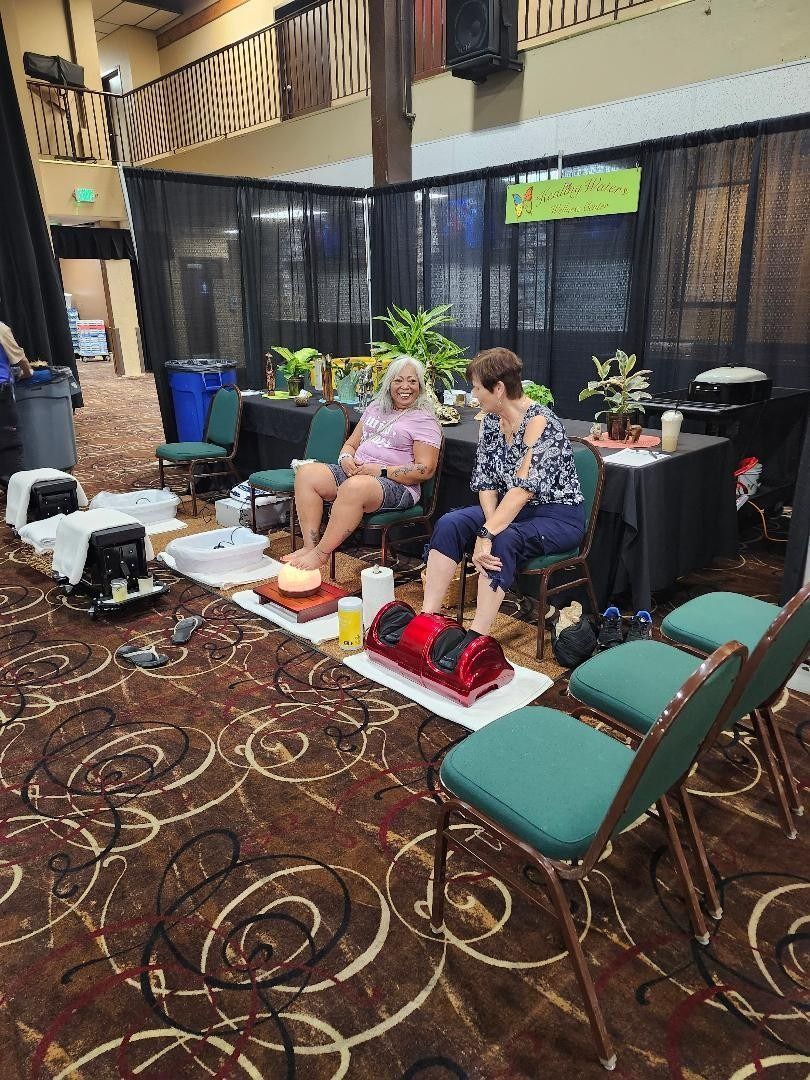 Two people seated at a booth in a convention hall, with display tables and banners nearby.