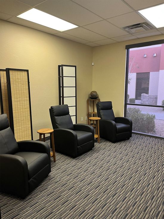 Waiting room with three black recliners, patterned carpet, and a large window with daylight.