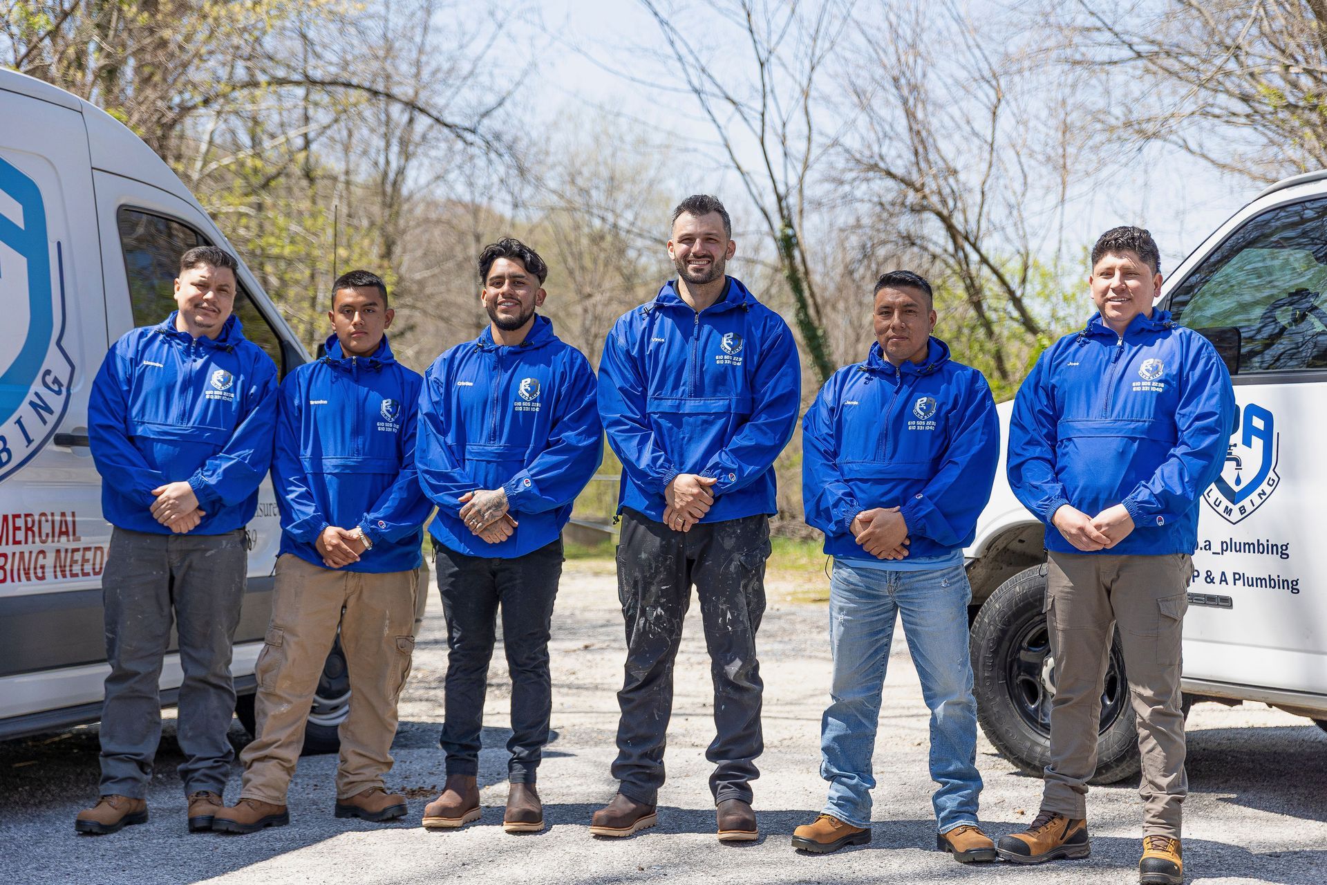 Six people in blue jackets standing outdoors beside a white van on a sunny day