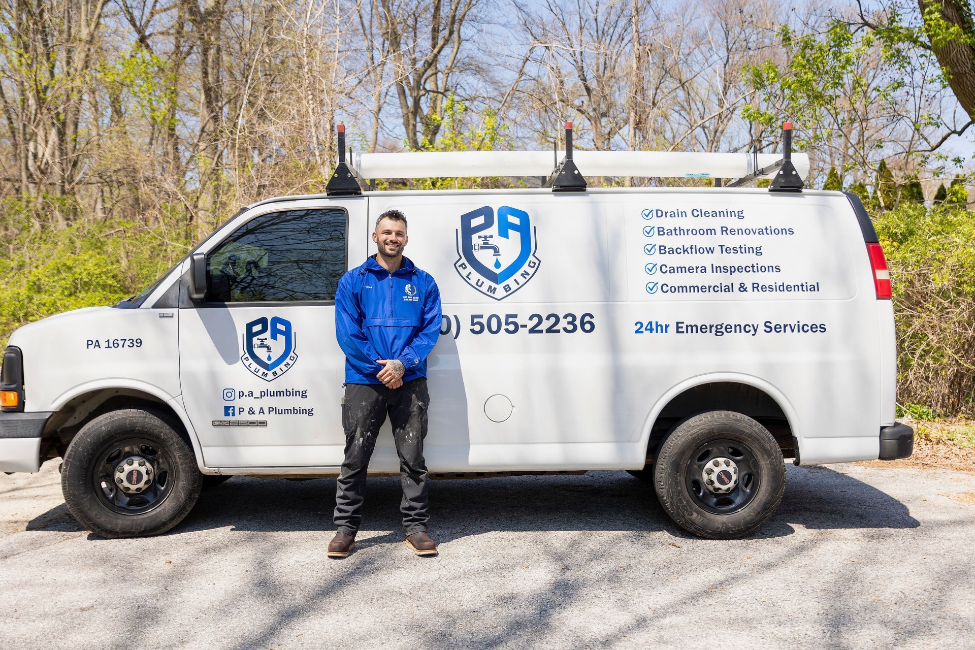 Man standing beside a white service van with blue logos and contact info on a roadside.