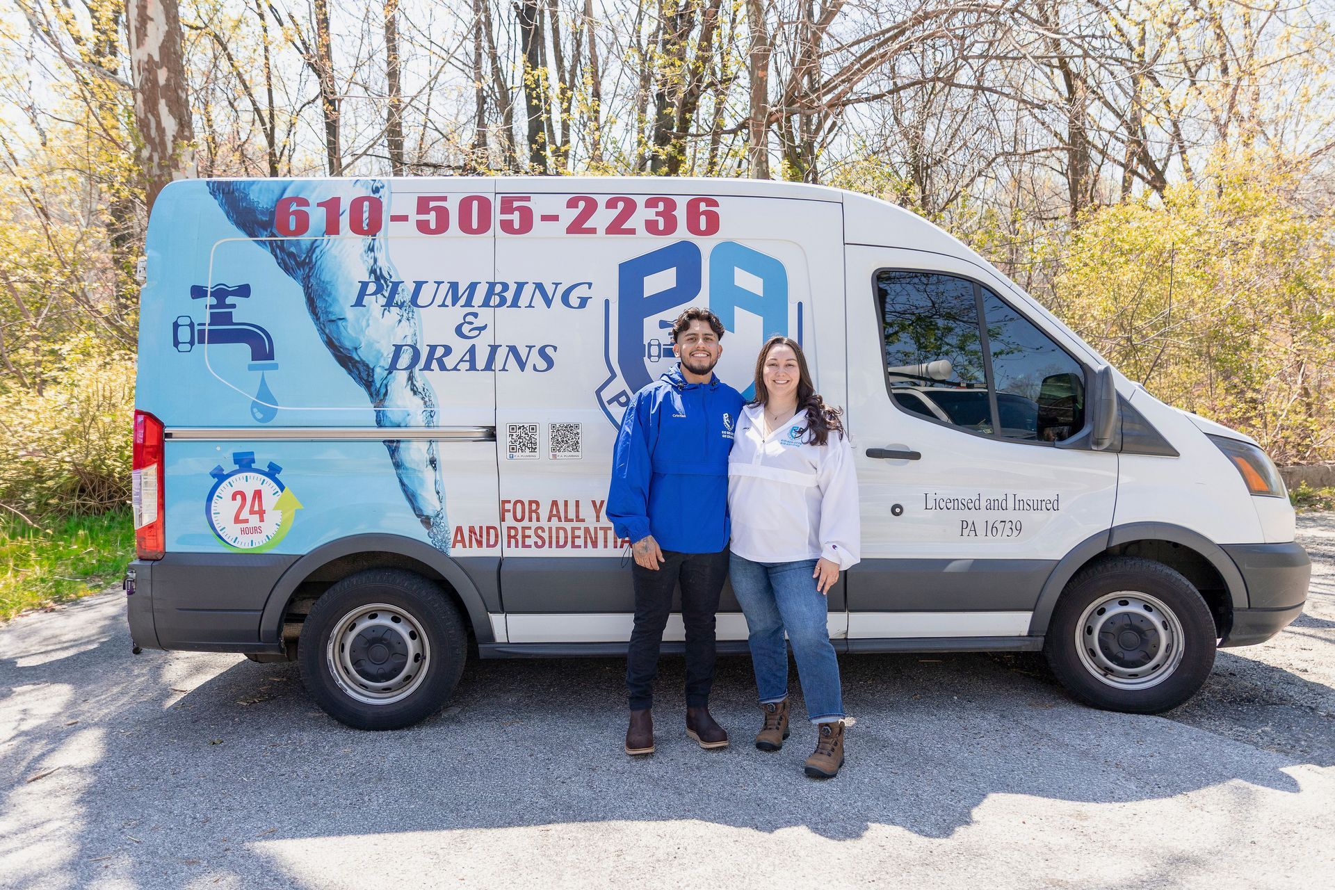 Two people stand beside a white plumbing service van in a sunny outdoor lot.