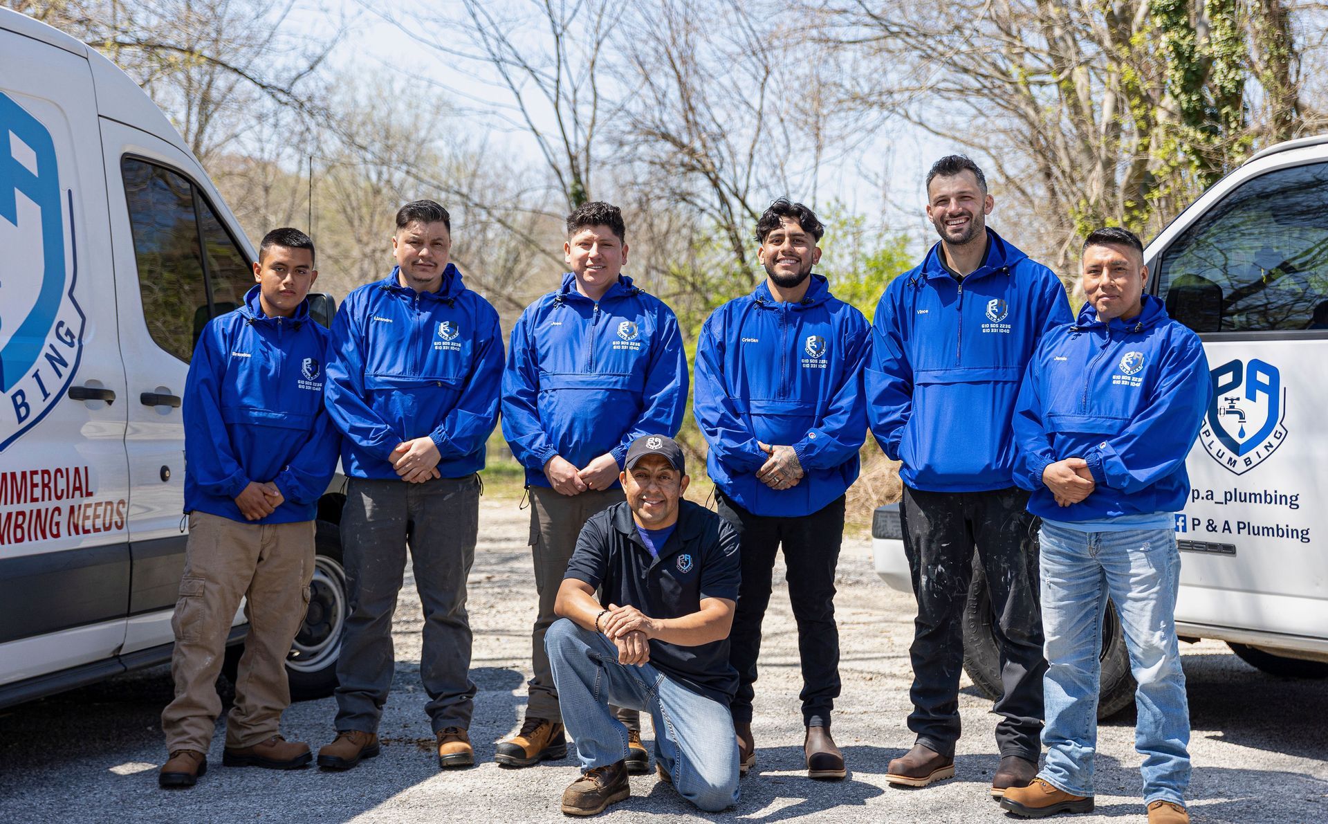 Seven people in blue jackets posing beside a company van outdoors on a sunny day