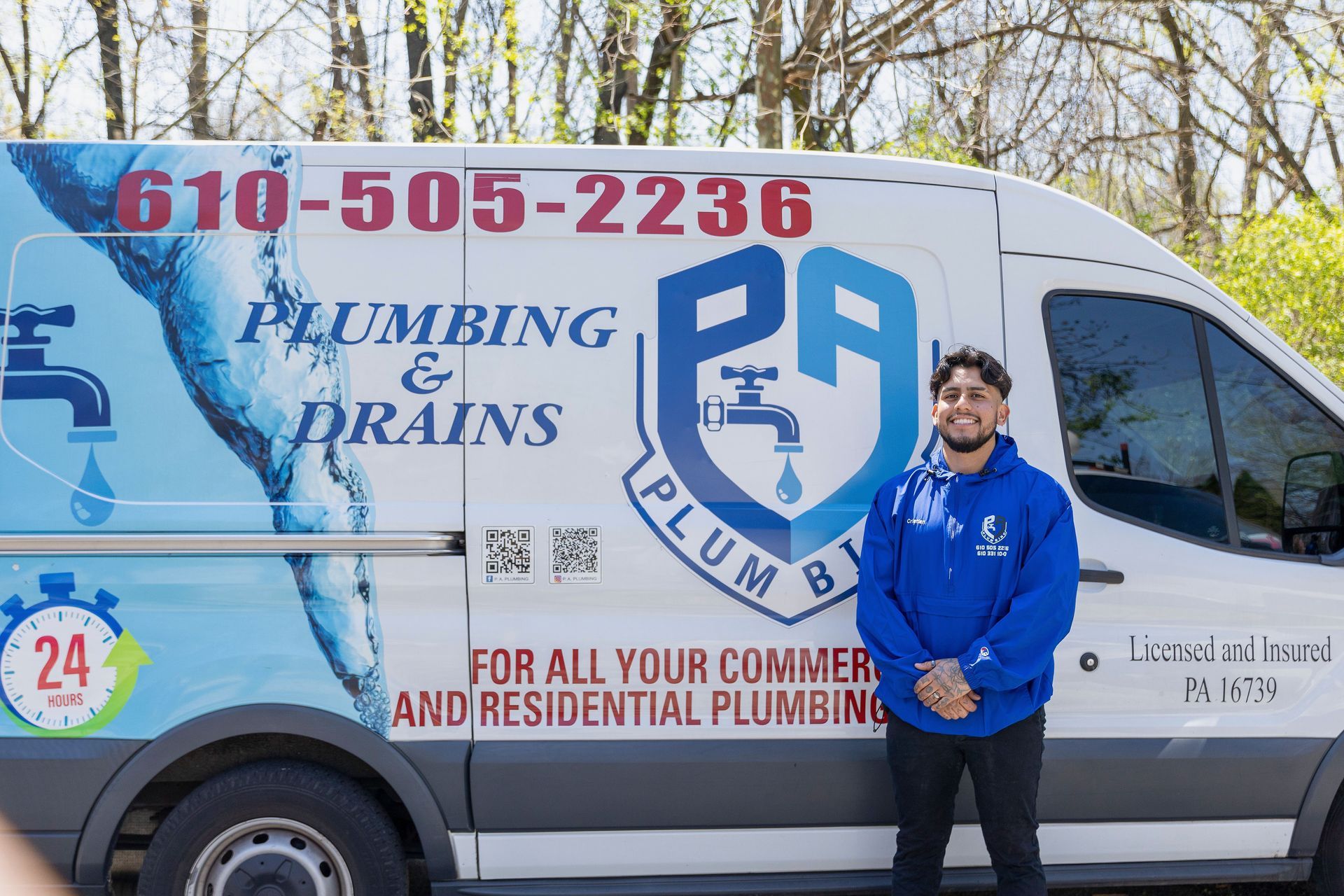 Plumbing service van with logo and phone number, man in blue hoodie standing beside it.