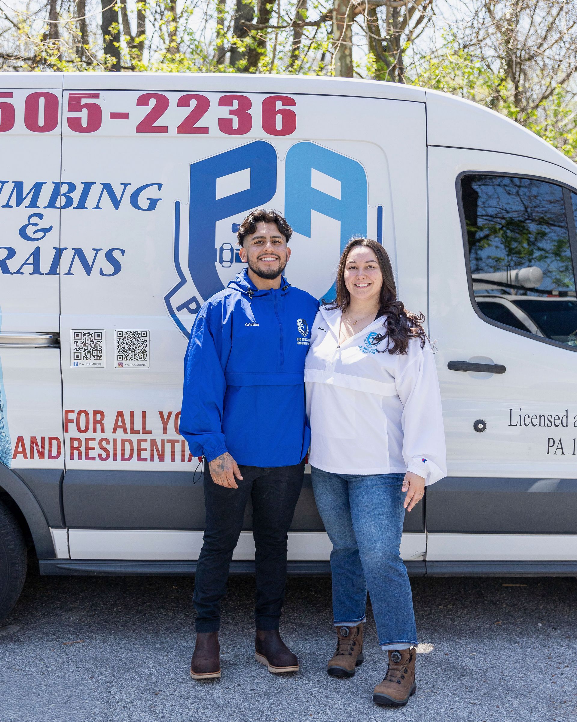 Two people standing in front of a white plumbing service van, smiling outdoors.