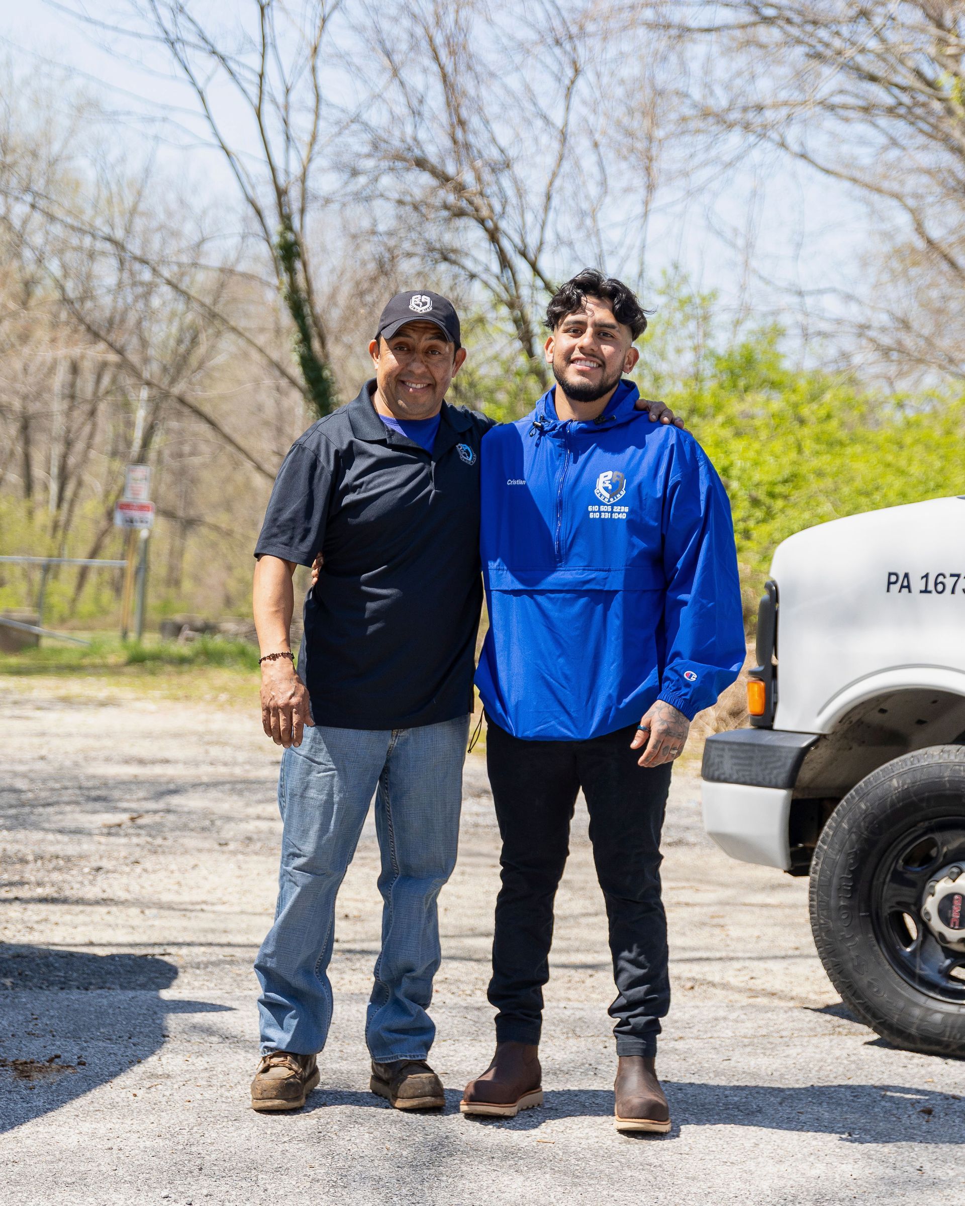 Two people standing outdoors beside a white truck, smiling in casual clothes.