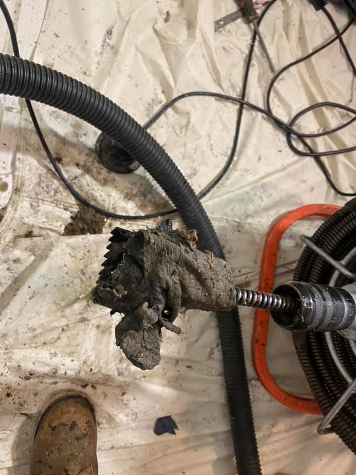 A drain snake with a large, dirty clog attached, resting on a white sheet in a work area.