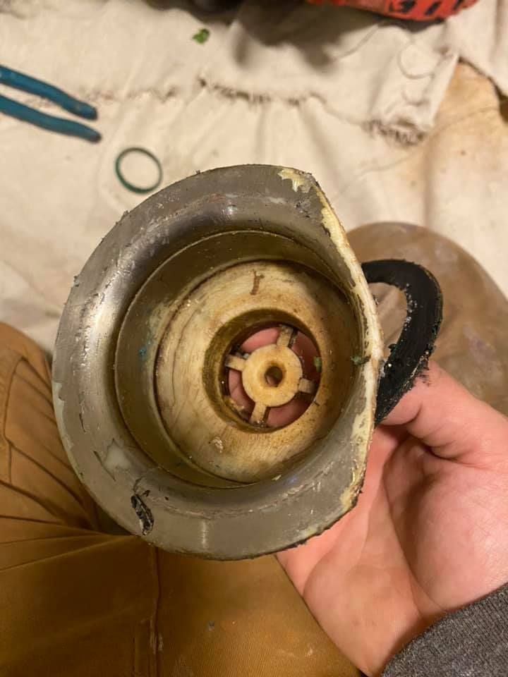 Hand holding a dirty metal mechanical part with a black handle on a beige cloth surface