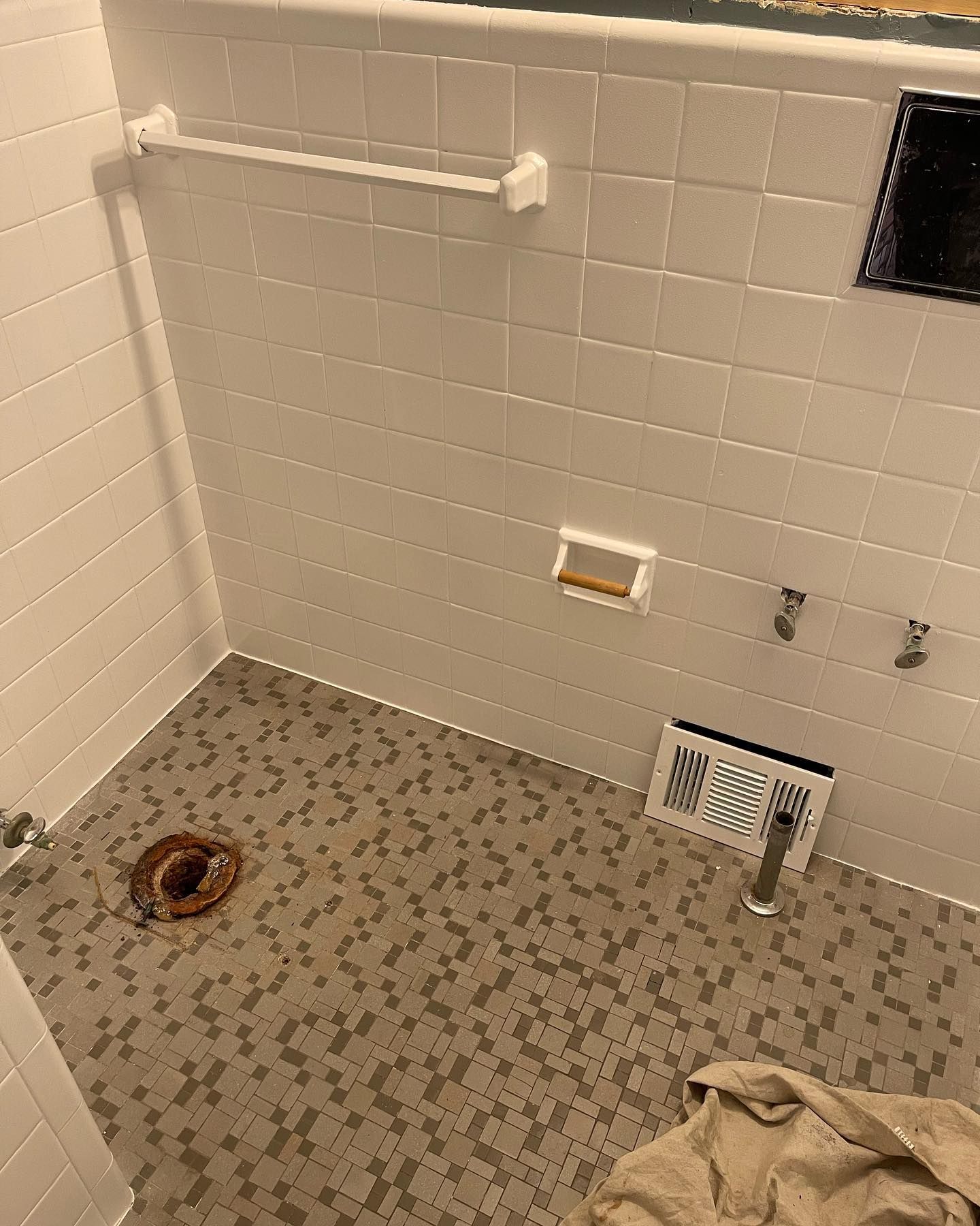 Small tiled bathroom with shower grab bar, floor drain, wall fixtures, and a vent fan panel.