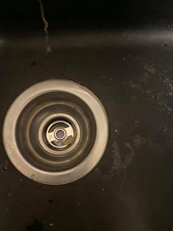 Circular metal sink drain in a dark sink basin with water stains.