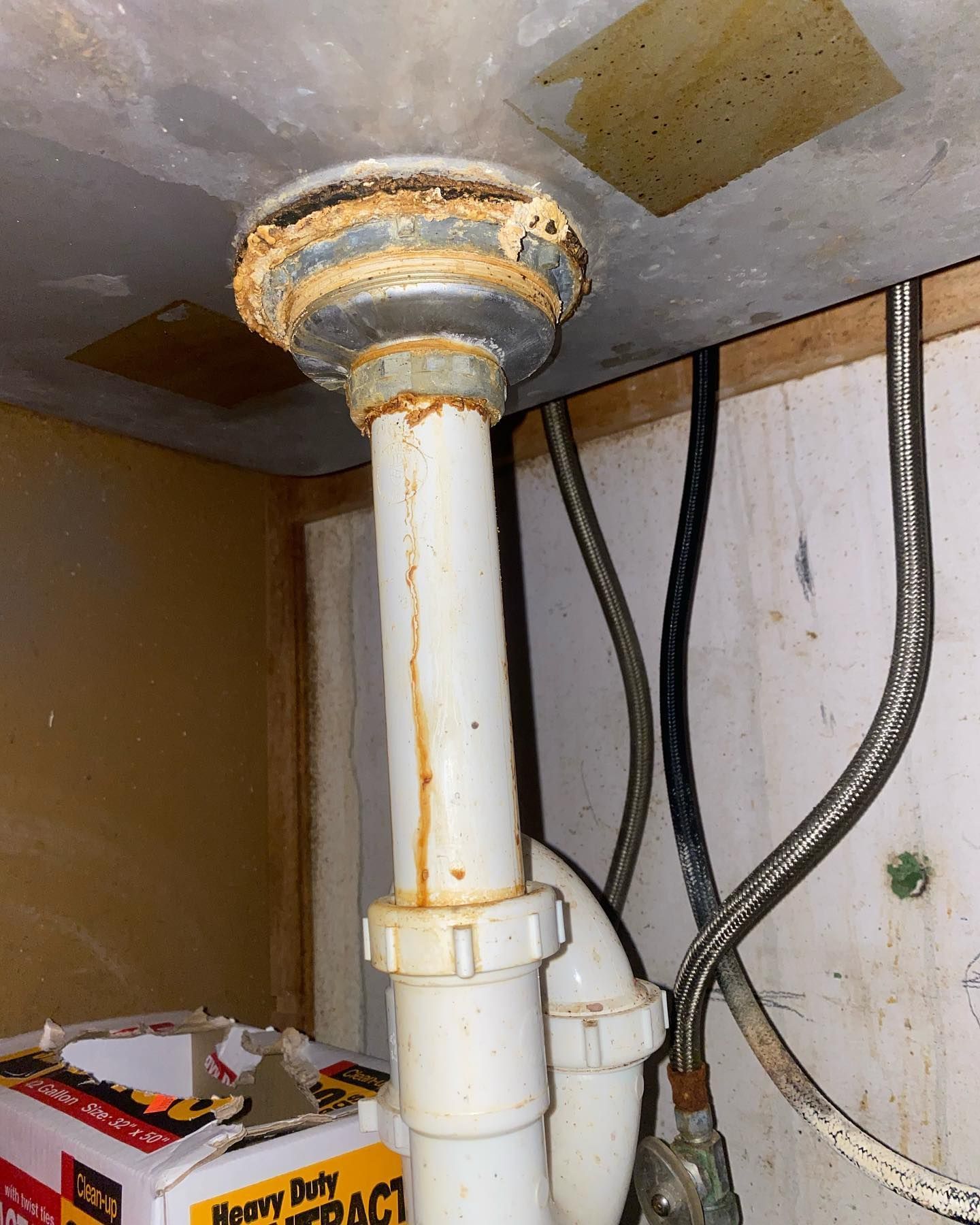 Under-sink plumbing with a rust-stained white drain pipe and a black hose against a cabinet wall