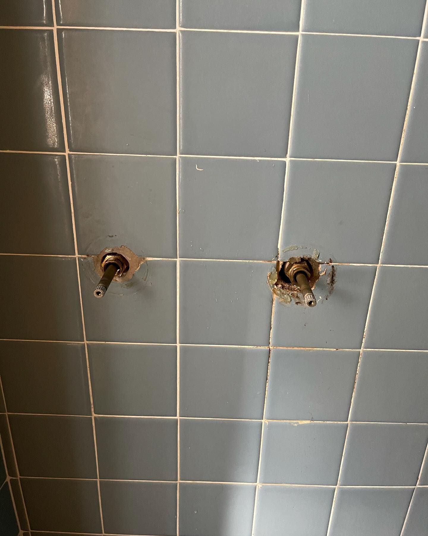 Two metal pipes protruding from blue tiled wall with white grout.