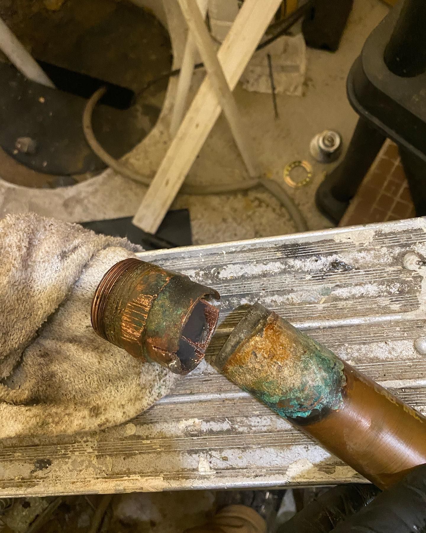 Burnt, corroded metal pipe joint with blue-green oxidation on a worn workbench