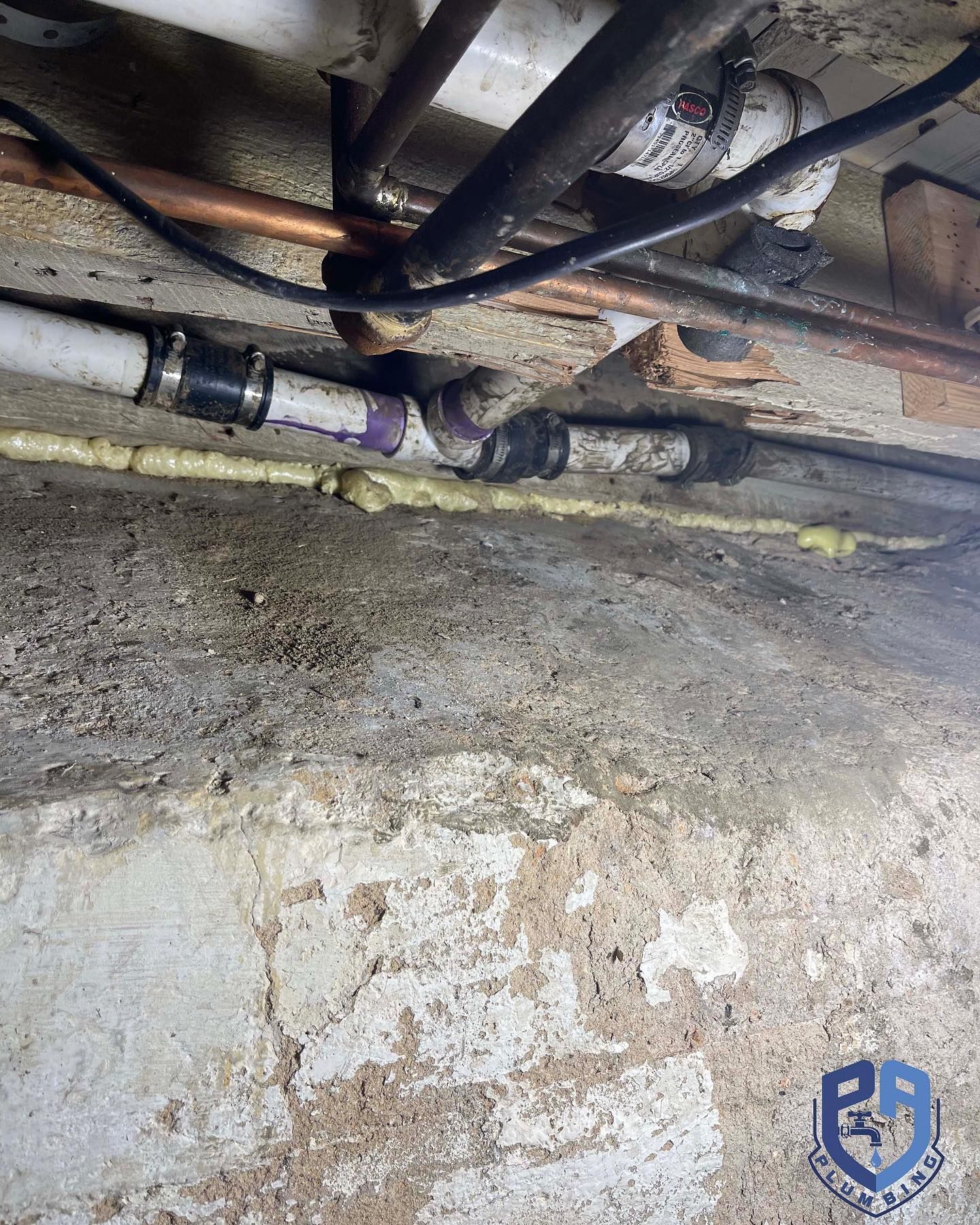 Rusty pipes and a leaking valve under a concrete floor, with damp stains and debris.