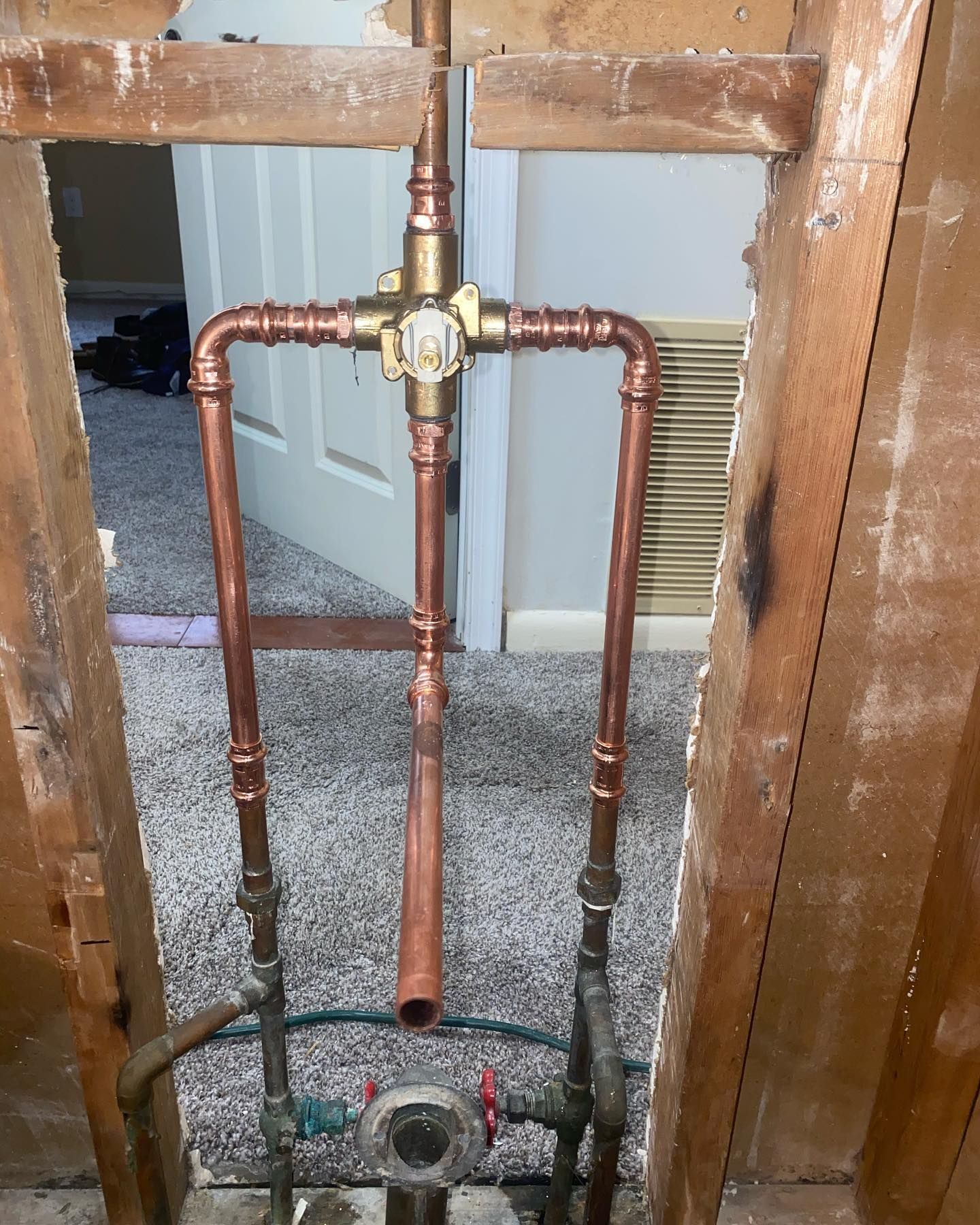 Copper plumbing pipes and valve inside an unfinished wall opening beneath a doorway.