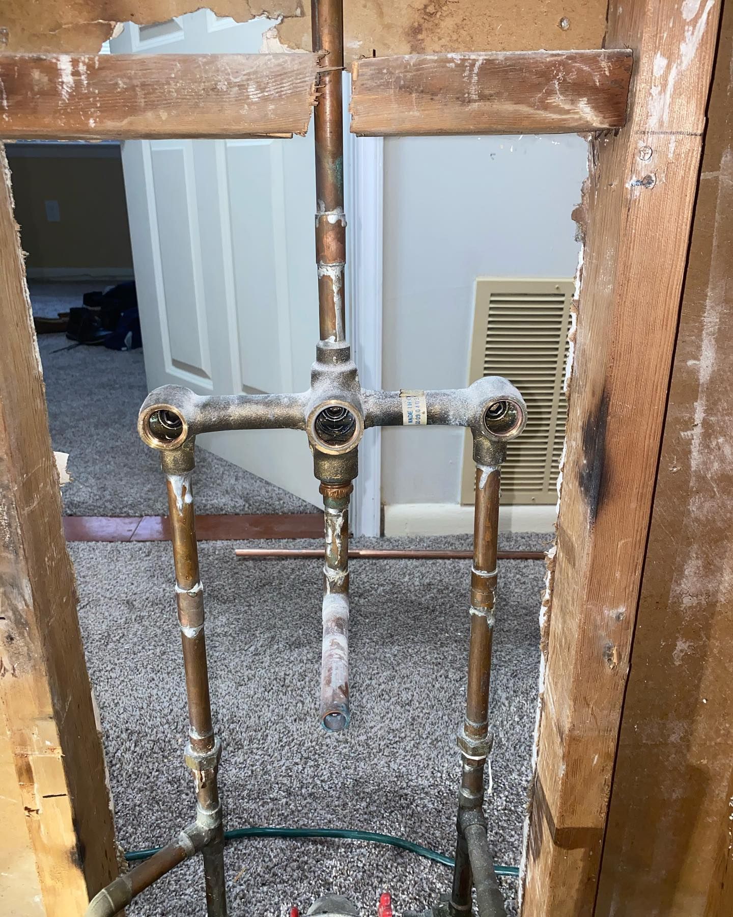 Plumbing pipes and valves framed by unfinished wooden studs in a construction area.