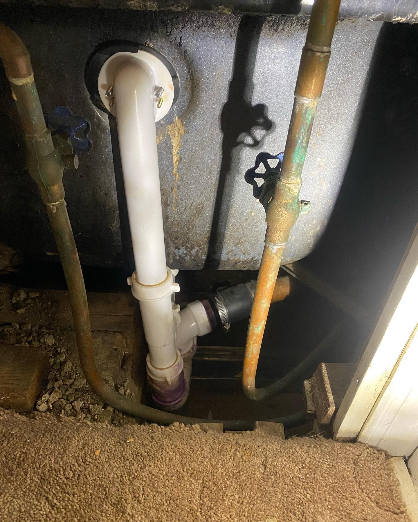Under-sink plumbing with white and copper pipes in a cramped, dusty cabinet opening