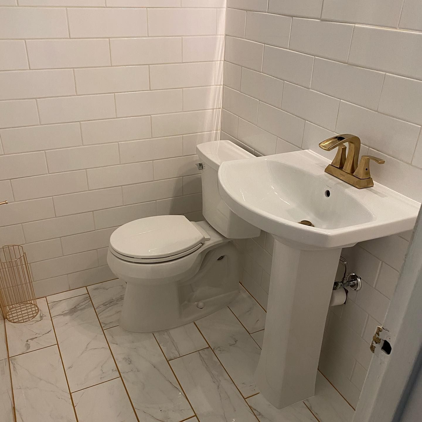Bathroom with white toilet, sink, and white tile walls and floor. Gold faucet.
