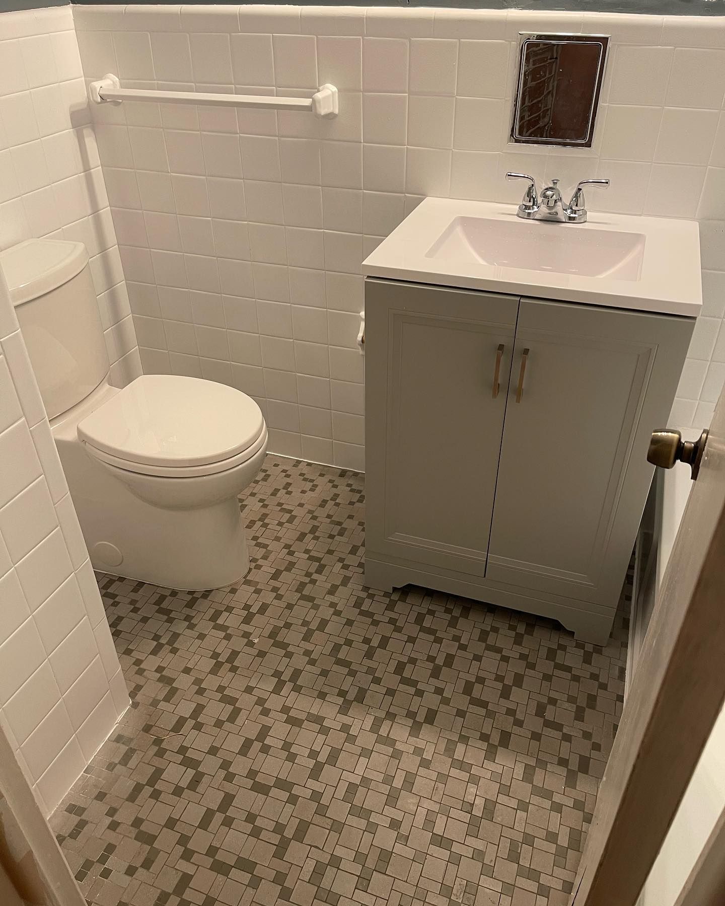 A small bathroom with a toilet, sink, white vanity, and patterned tile floor.