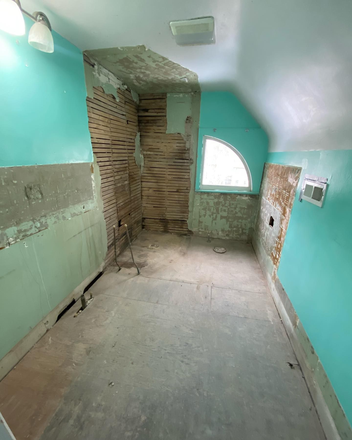 Bathroom renovation in progress, aqua walls, exposed wood studs, concrete floor, arched window.